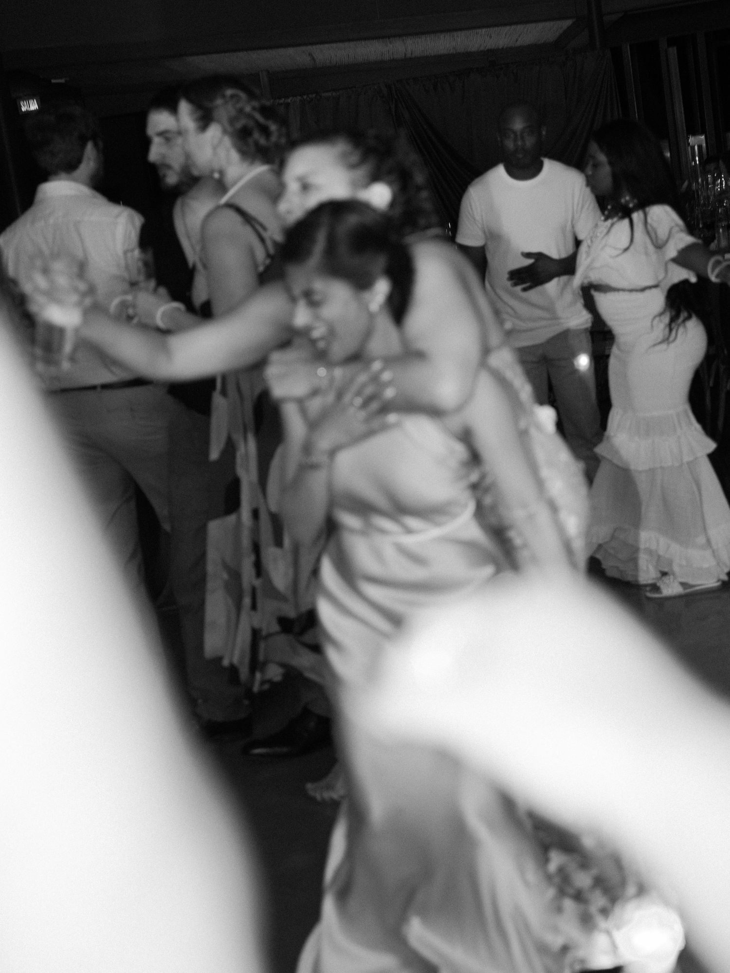 Black and white photo of guests dancing and celebrating at a lively wedding reception.