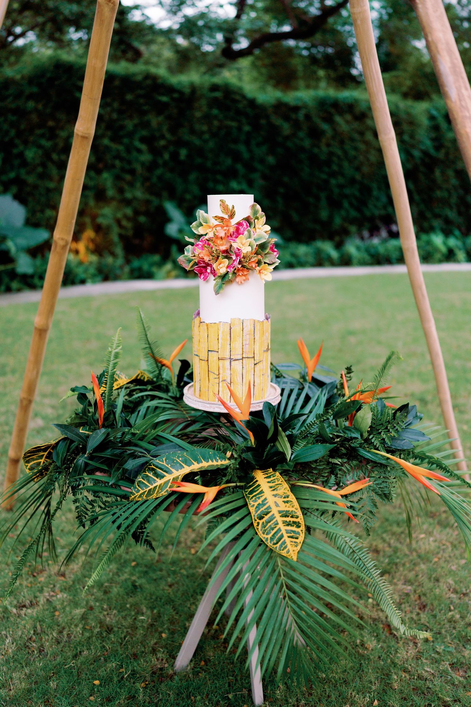 Tropical wedding cake display with palm fronds and bamboo decor elements.