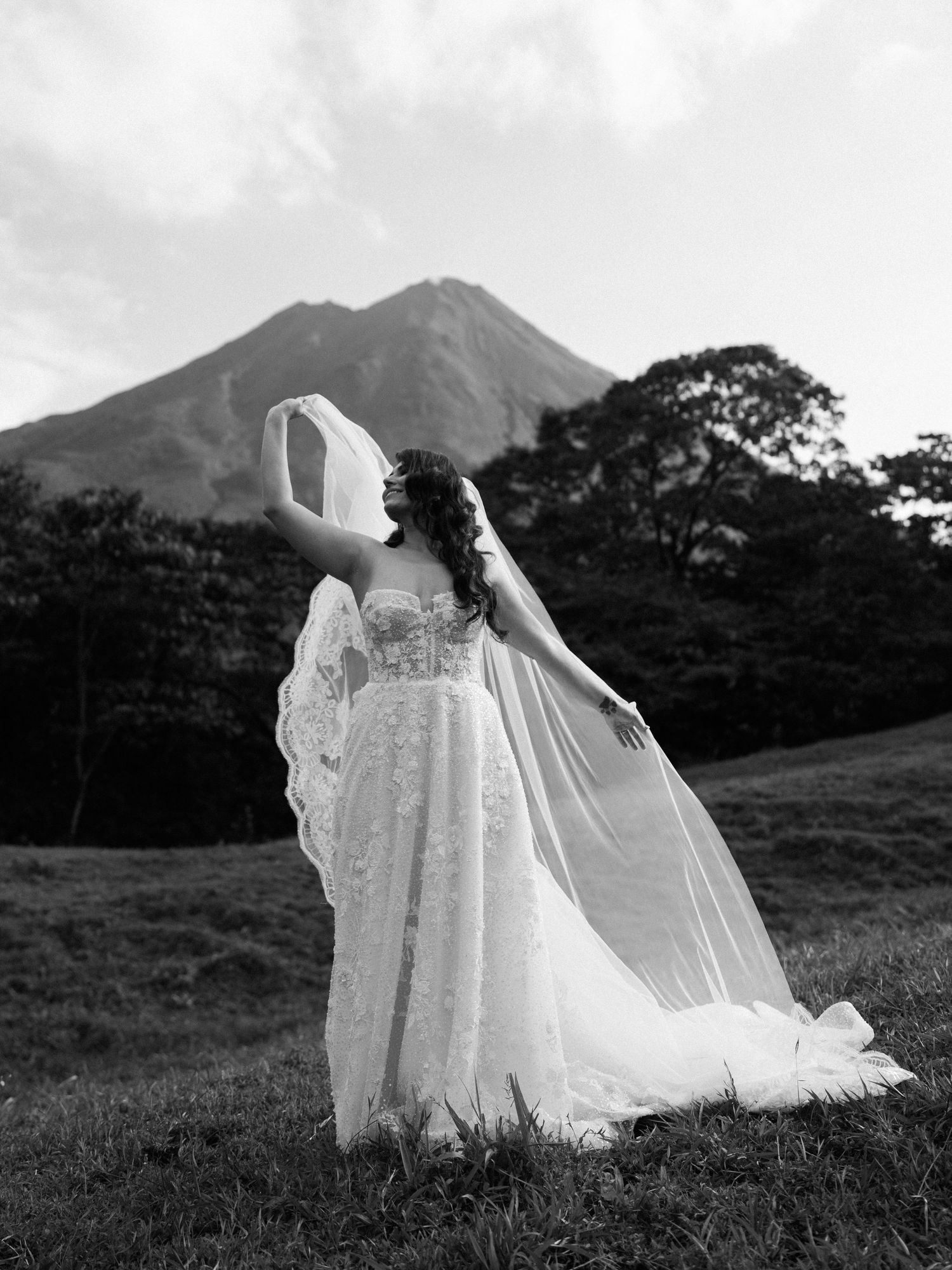 Dramatic black and white photo of wedding dress flowing in the wind against mountain backdrop.