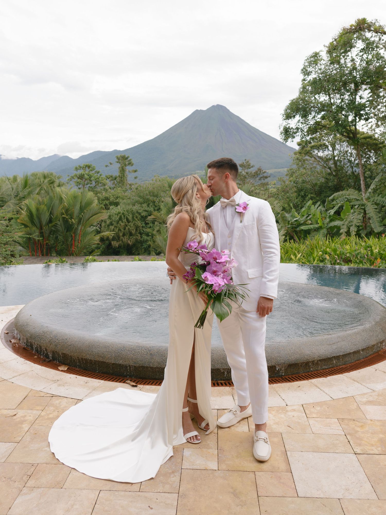 Wedding couple poses on stone patio with mountain views and tropical landscape.