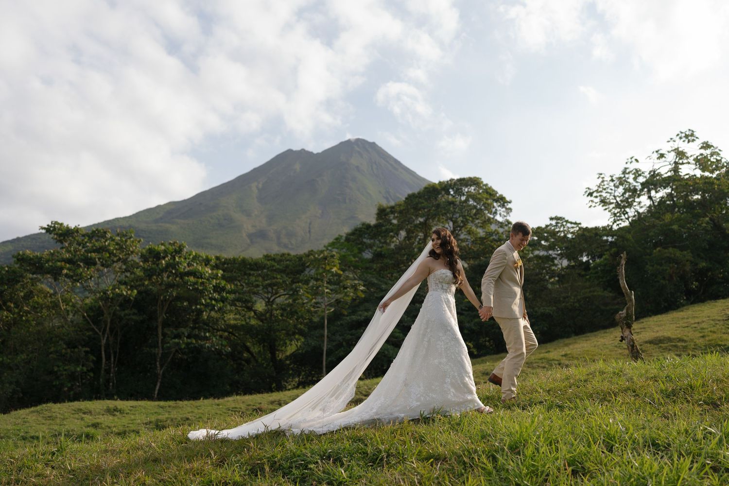 Wedding photography session on a green hillside with volcanic mountains in the background.