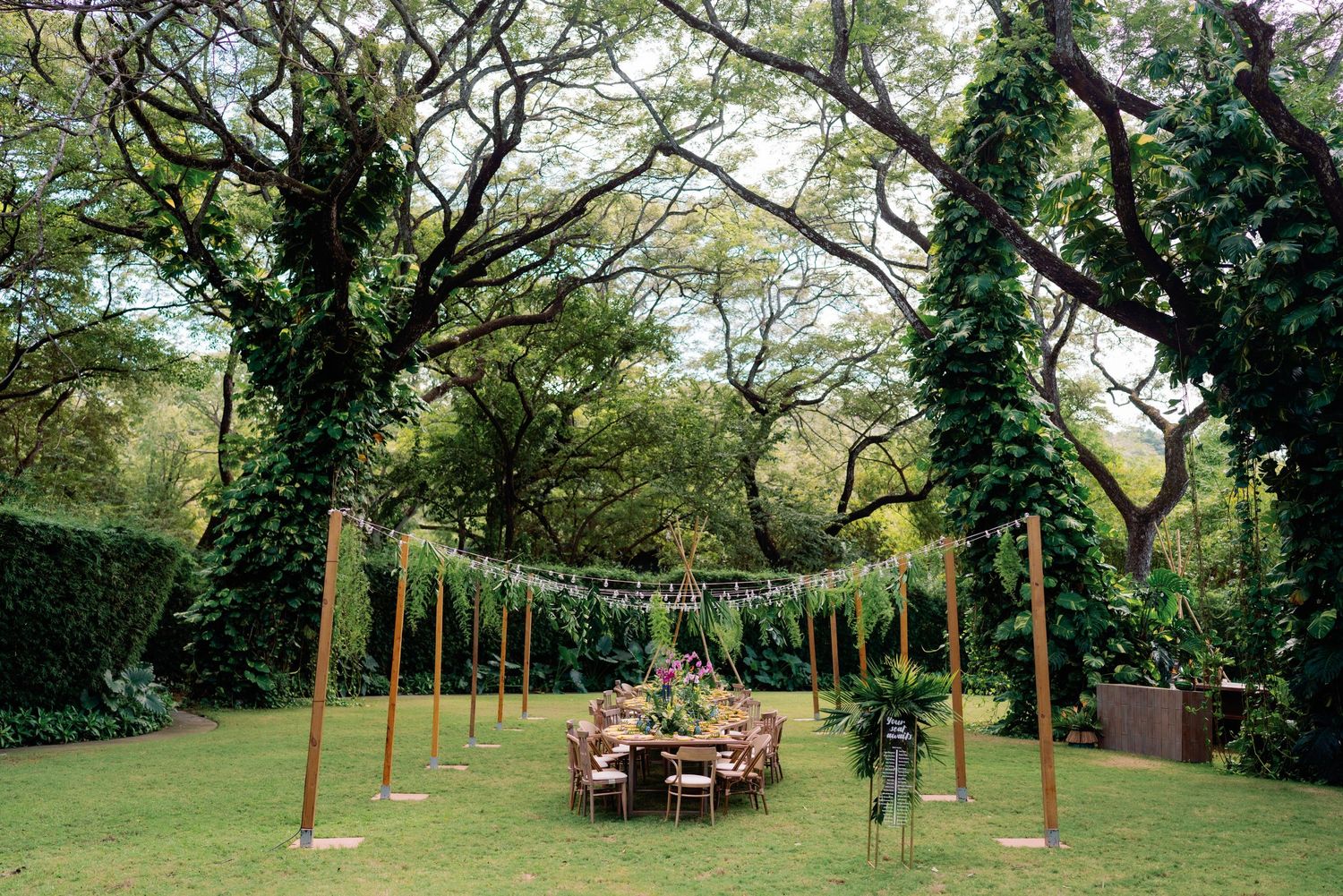 Panoramic view of an outdoor wedding reception setup with wooden posts and string lights.
