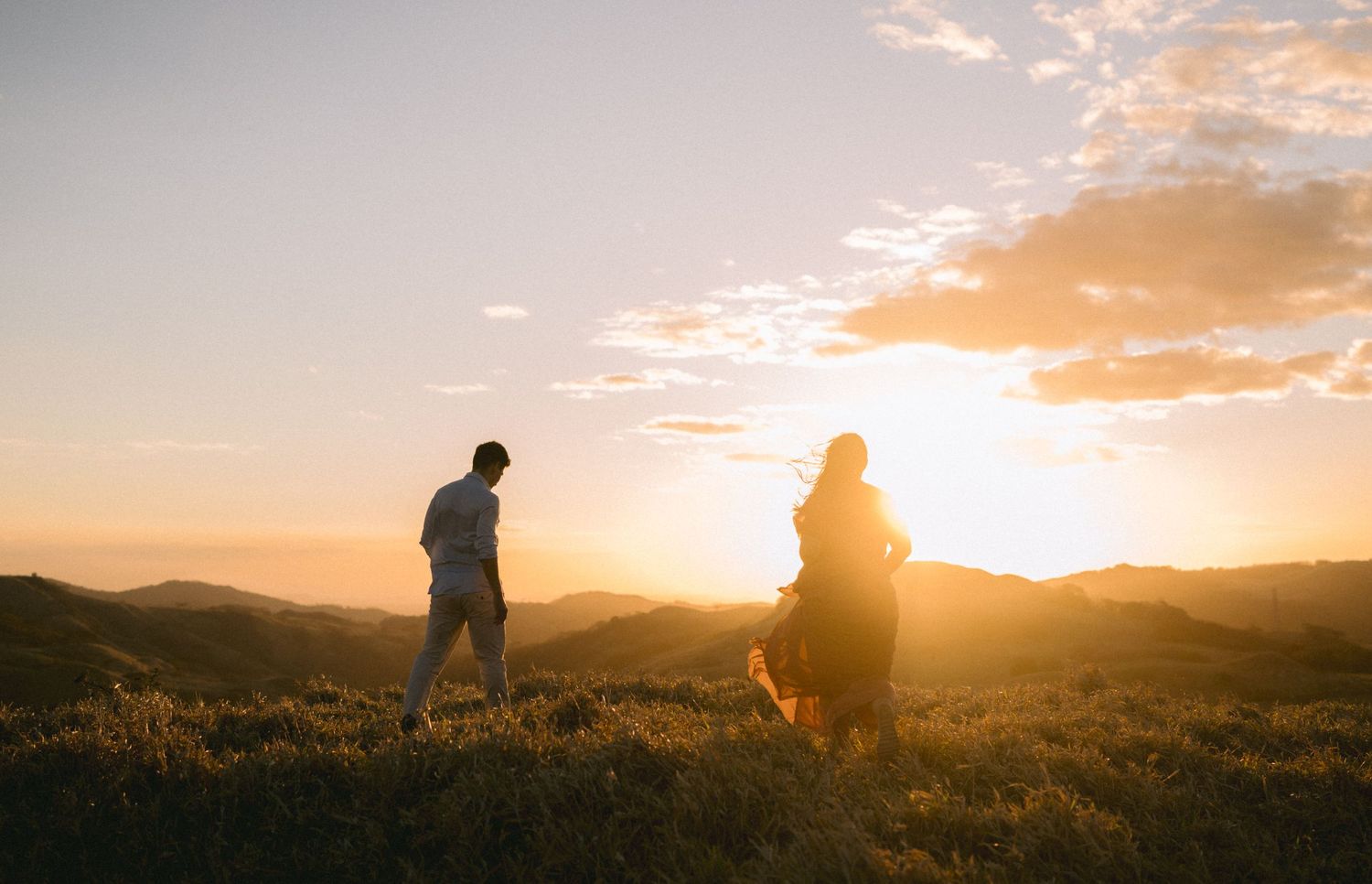Silhouettes of people against a dramatic sunset sky with mountains in the background.