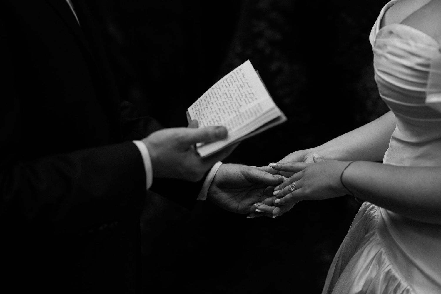 Black and white close-up of hands exchanging rings during wedding ceremony.