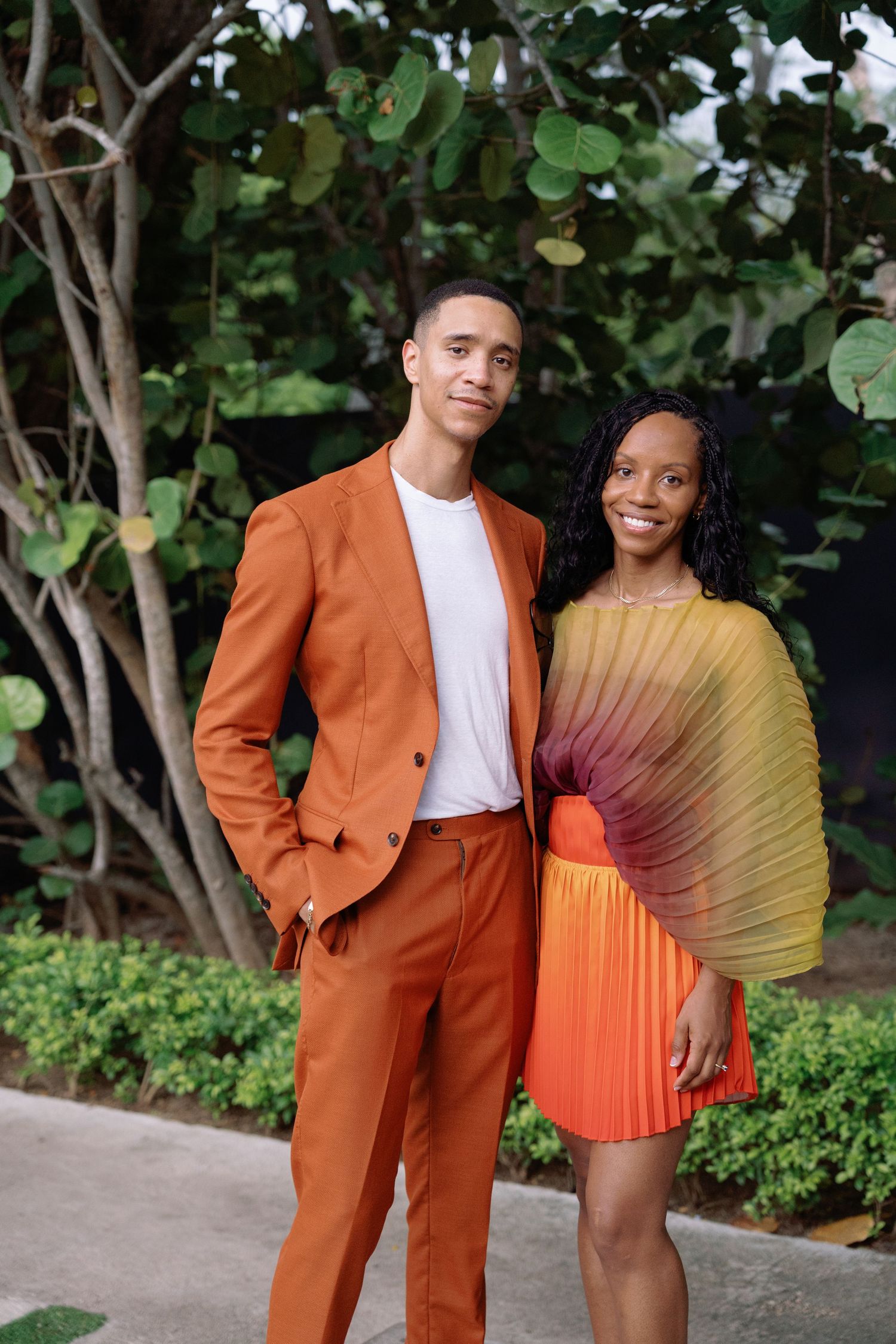 A couple poses outdoors wearing vibrant orange and yellow formal attire.