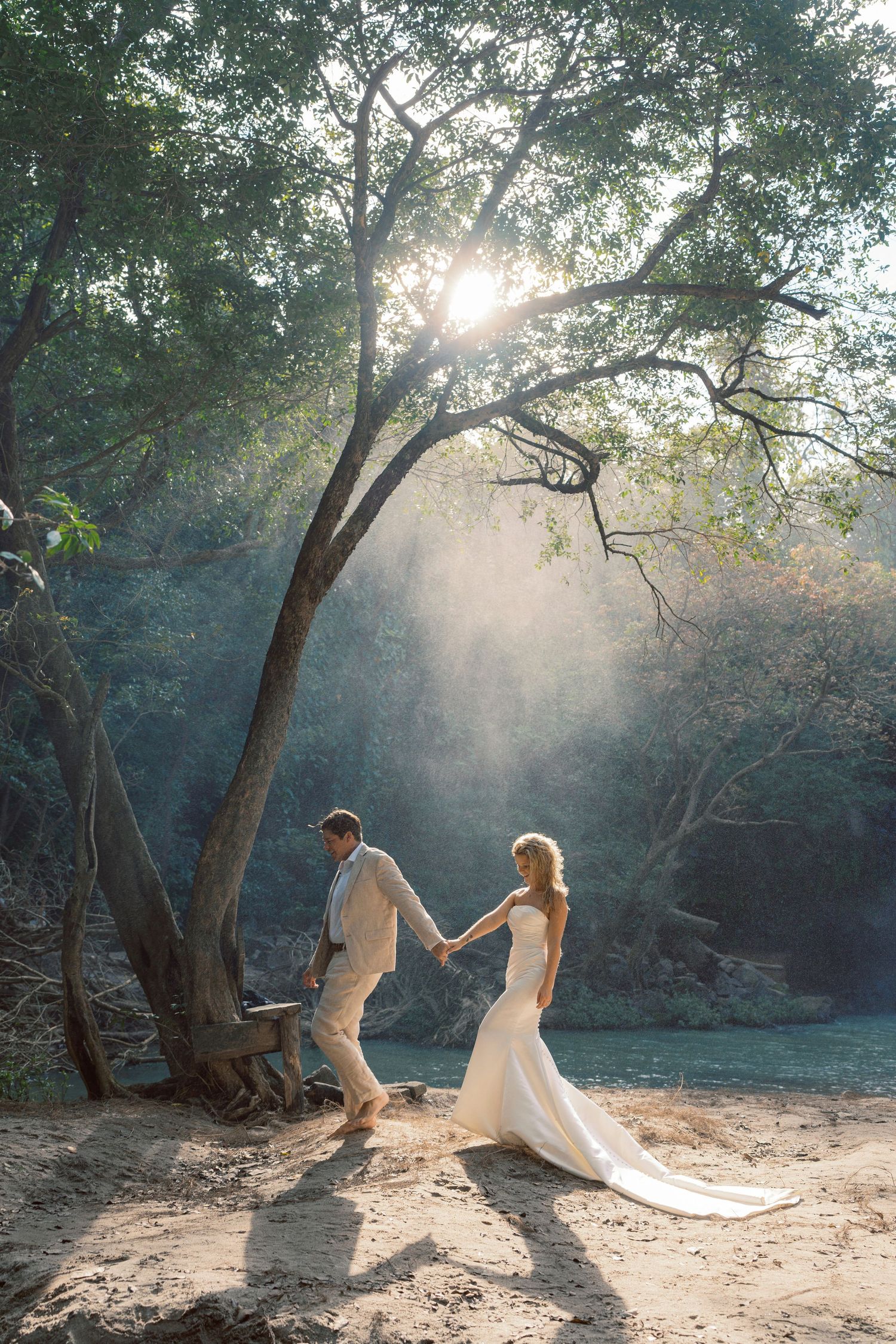 A couple in wedding attire dances together in a sunlit forest clearing creating a dreamy atmosphere.