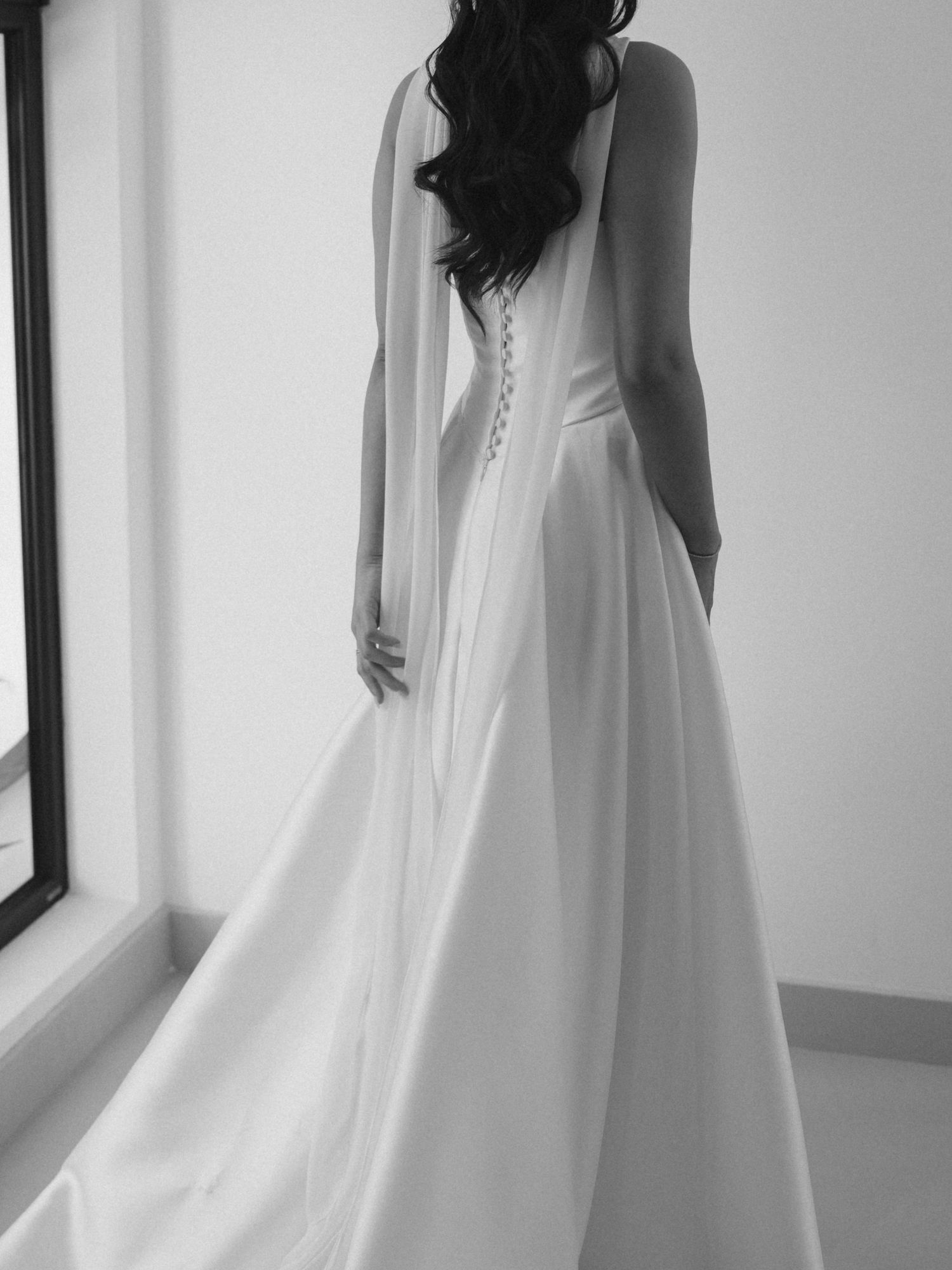 Black and white portrait of bride in flowing wedding dress near modern windows.