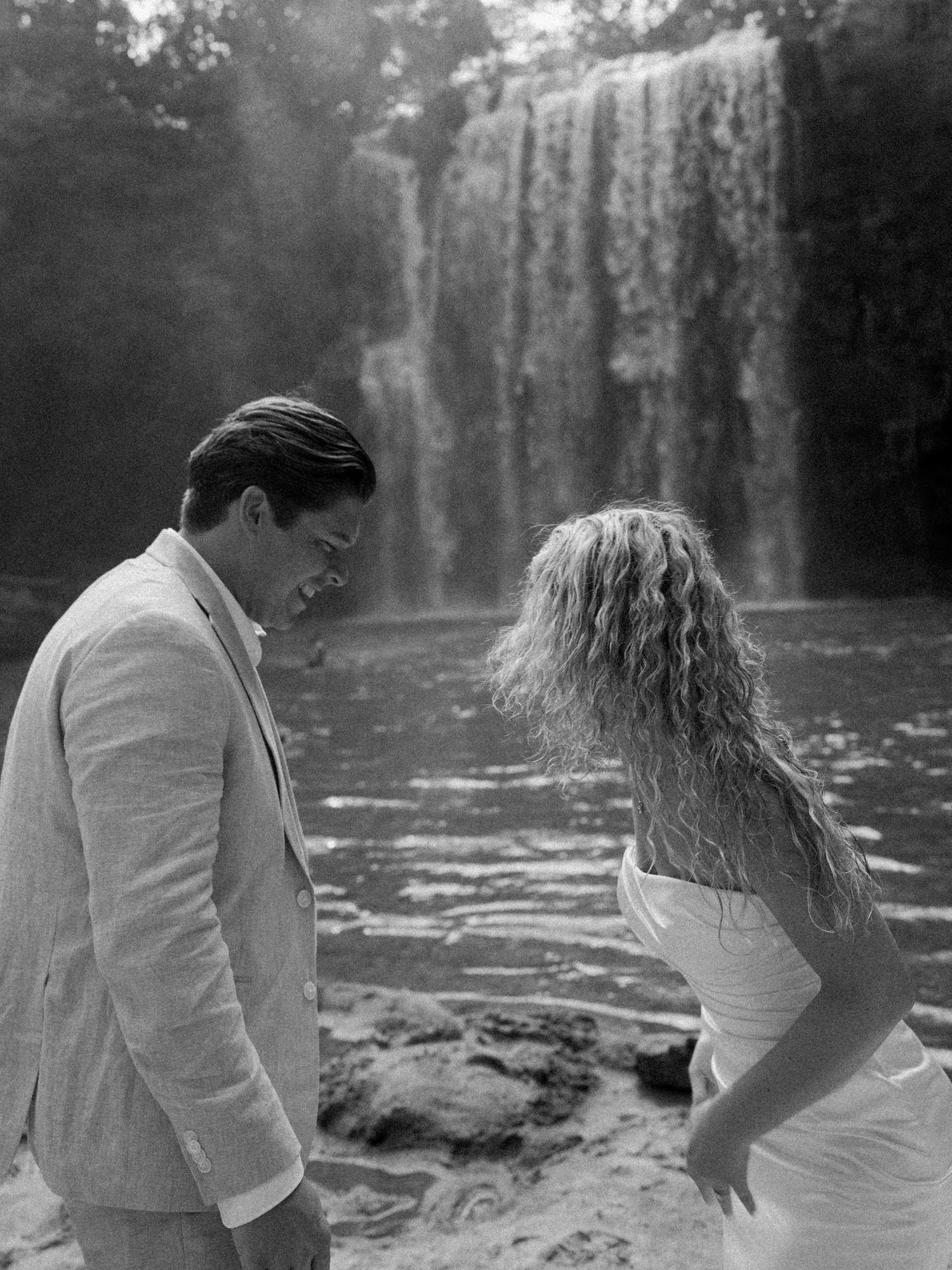 Black and white photo shows a tender moment by a scenic waterfall.