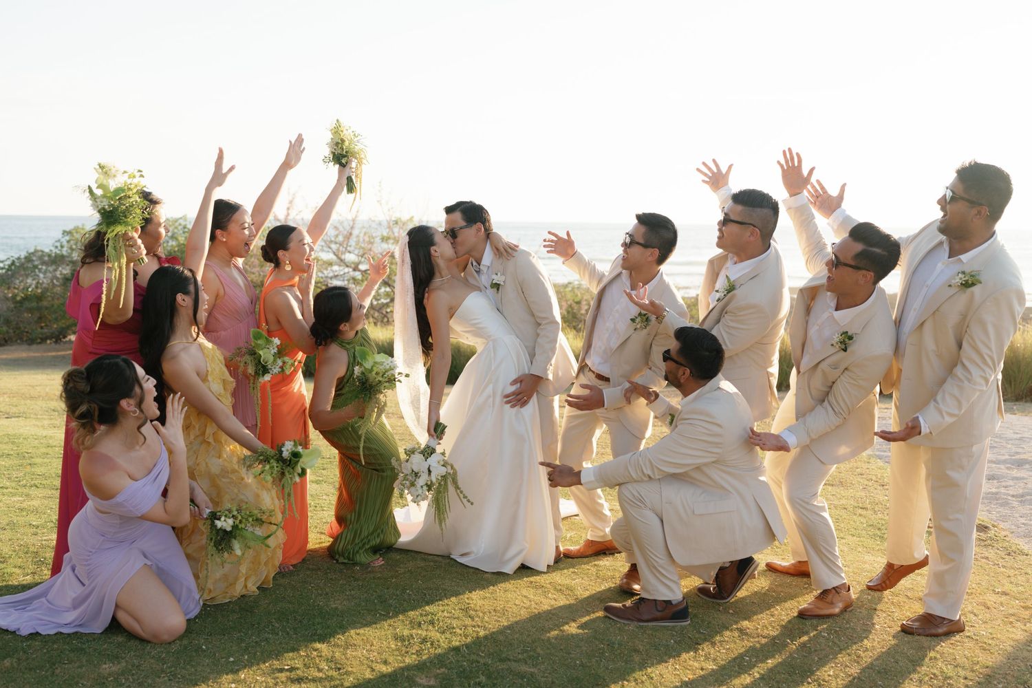Wedding party posing playfully on a grassy hill during golden hour celebrations.