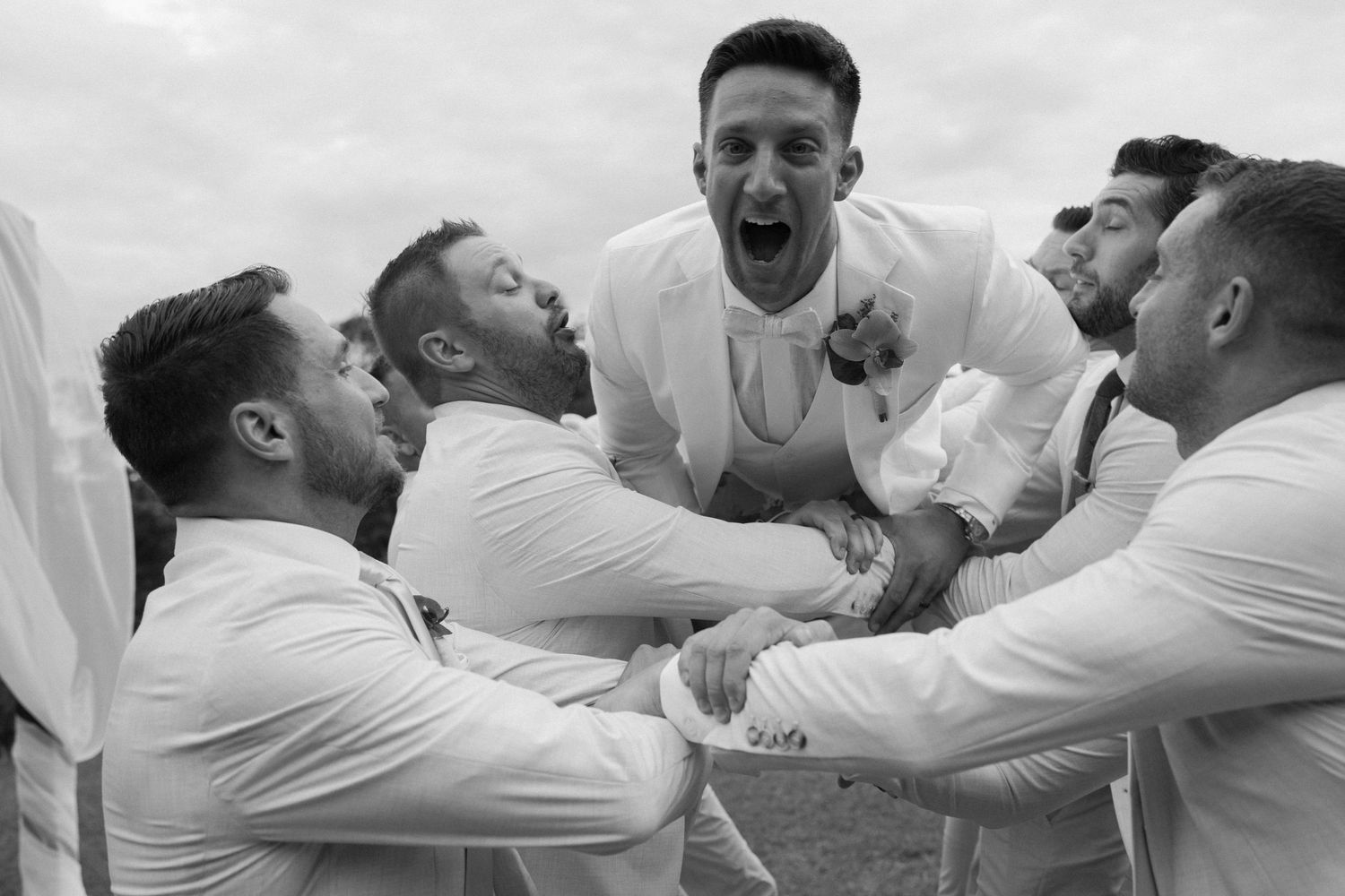 Black and white photo of groomsmen celebrating with excitement and laughter.