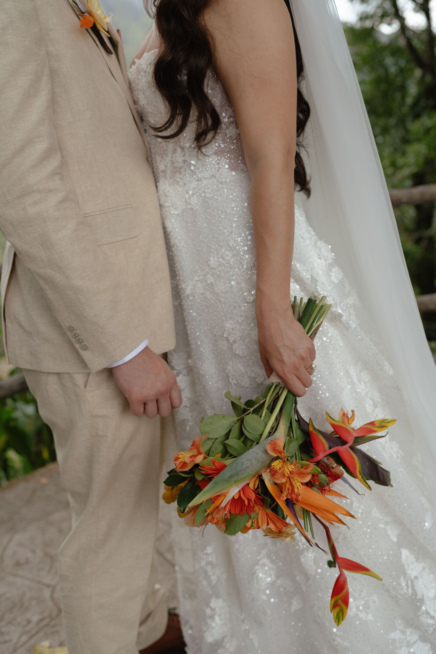 Detail shot of tropical orange and green wedding bouquet against white dress.
