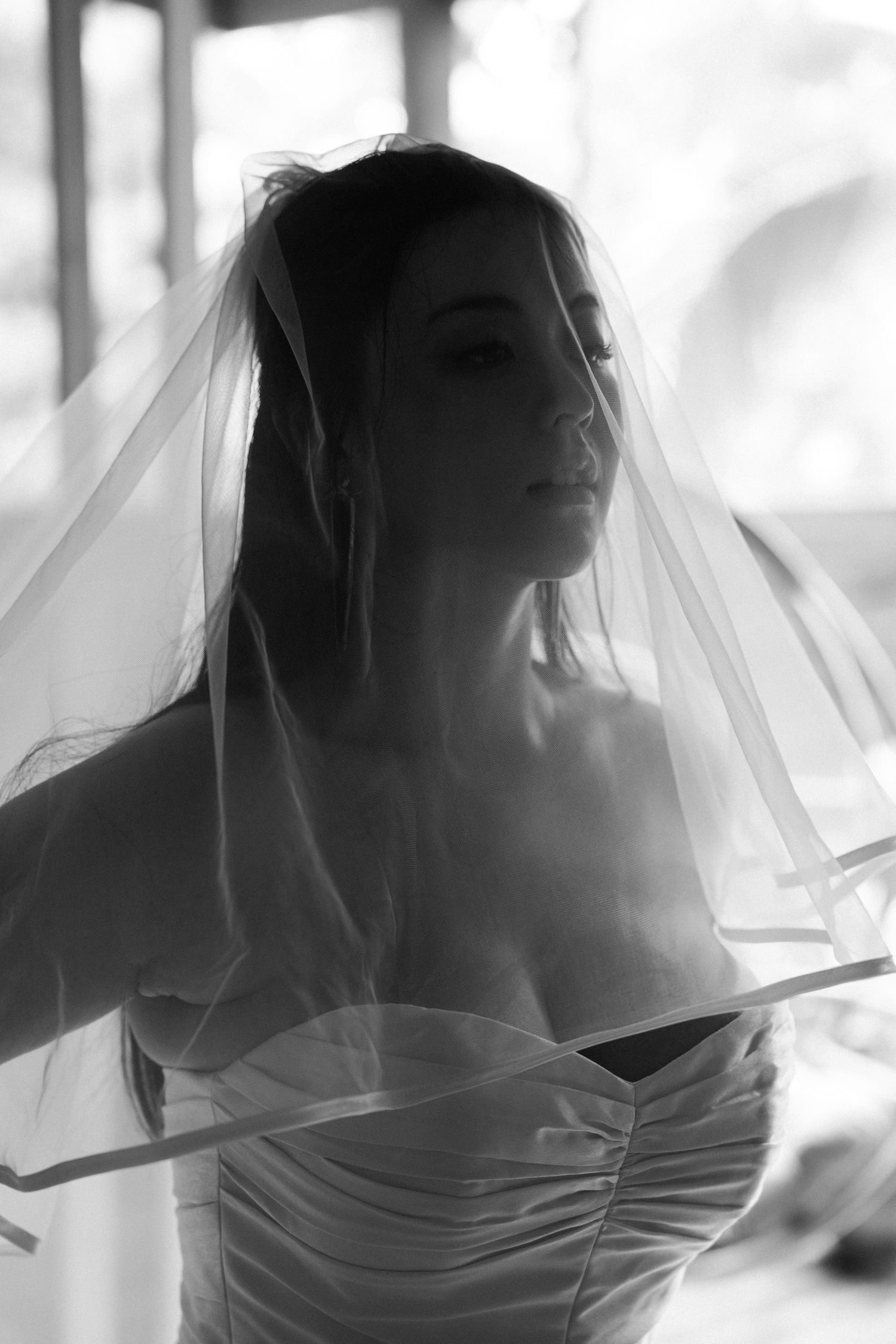 Artistic black and white portrait of bride with flowing veil in natural light.