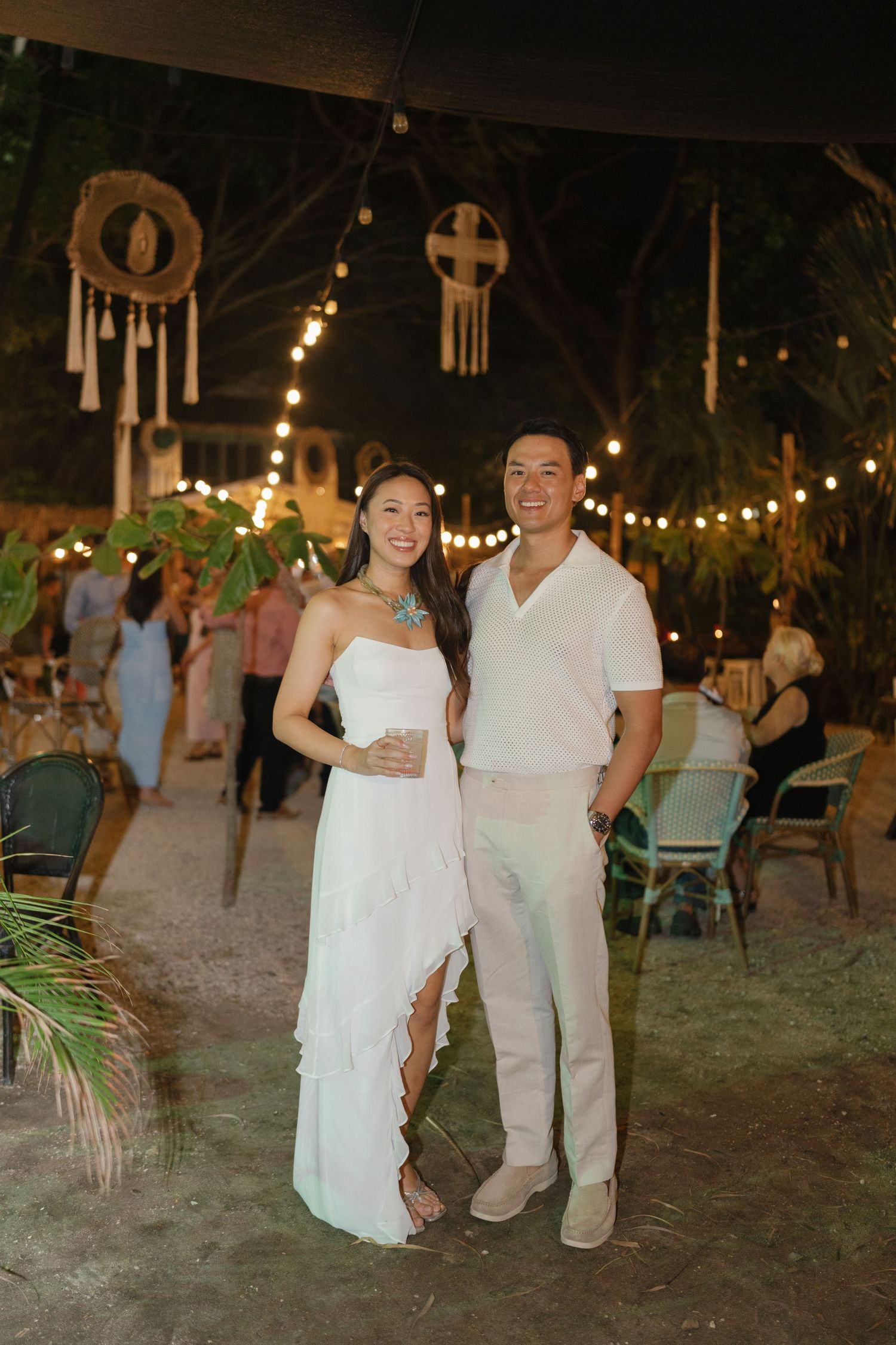 Couple dancing together on a sandy beach at night under string lights at a tropical wedding reception.