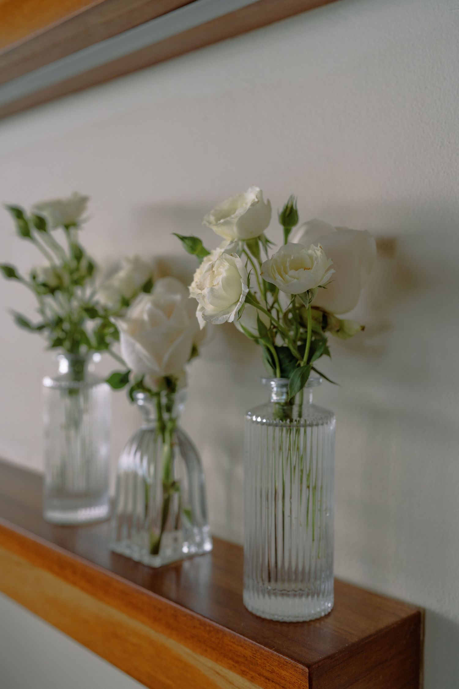 White flowers arranged in clear glass vases displayed on wooden shelves.