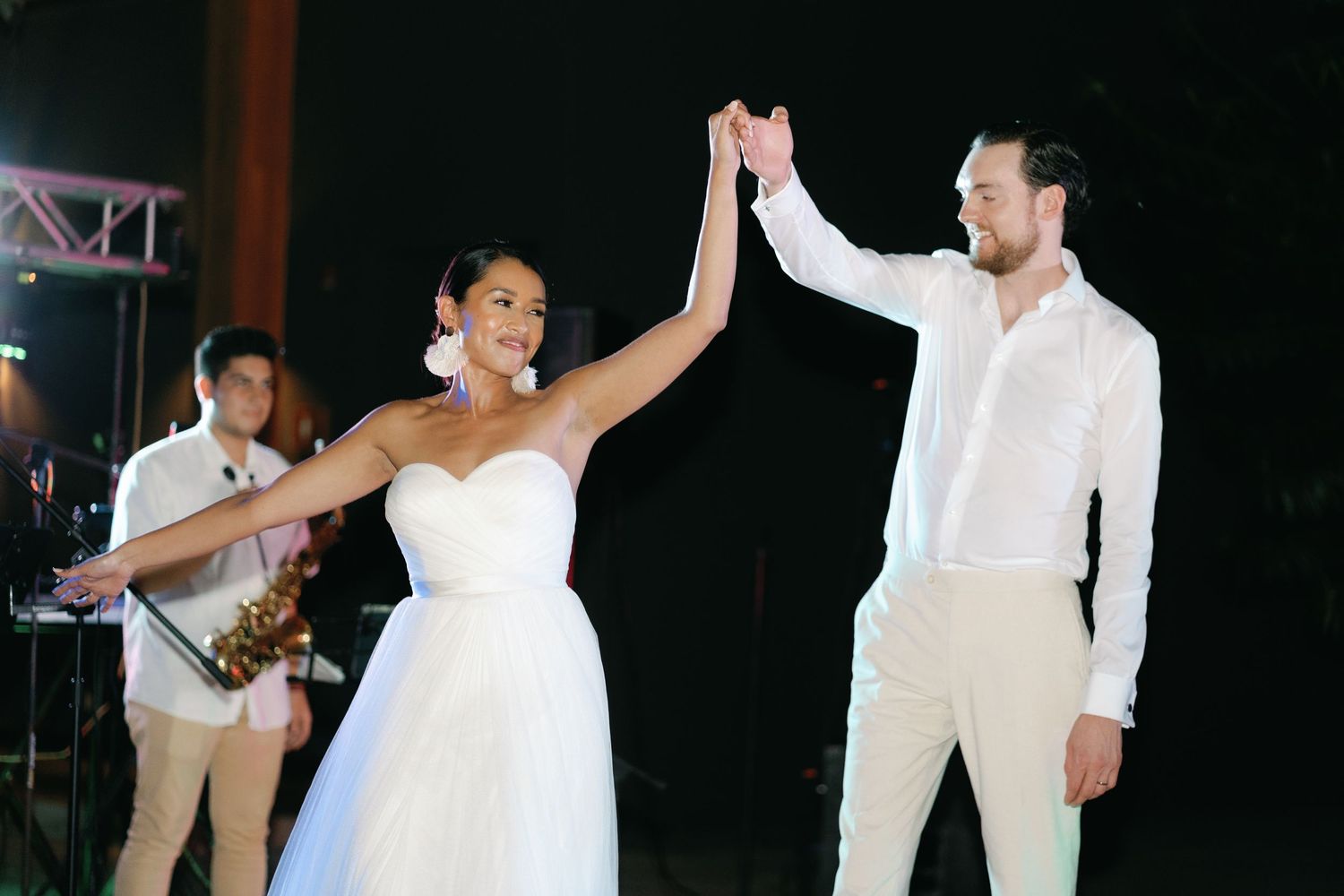 Dancing couples celebrating at nighttime wedding reception under twinkling lights.