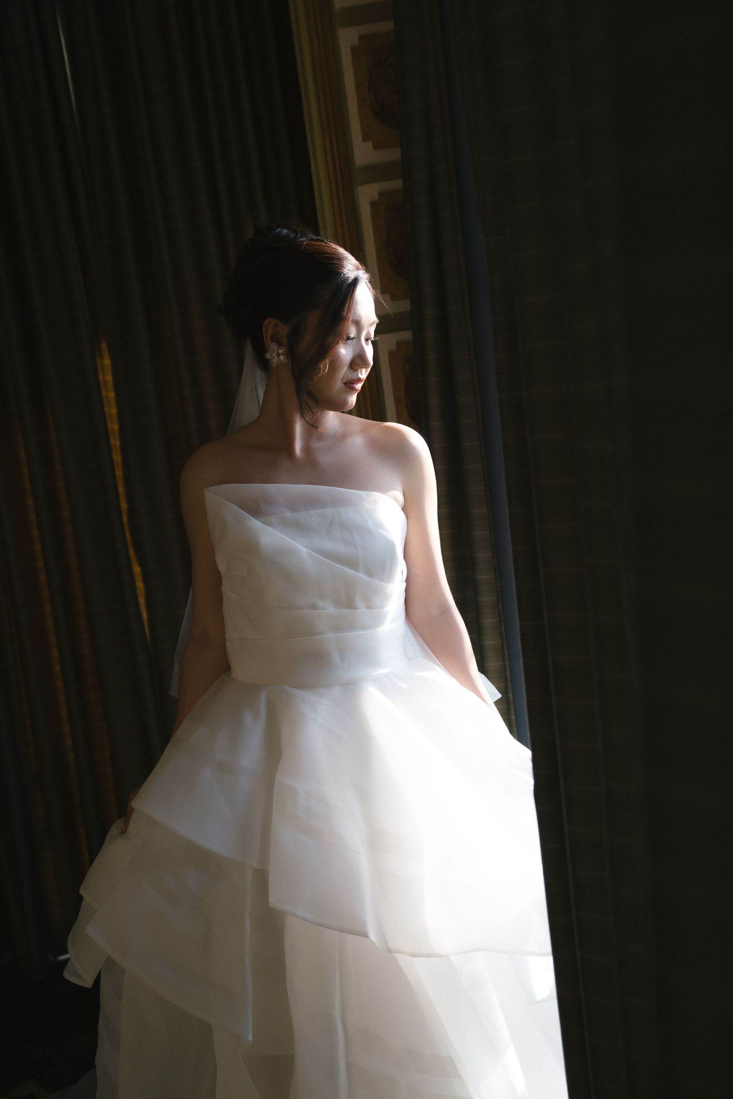 A flowing white wedding dress with layered tulle fabric captured in dramatic side lighting.