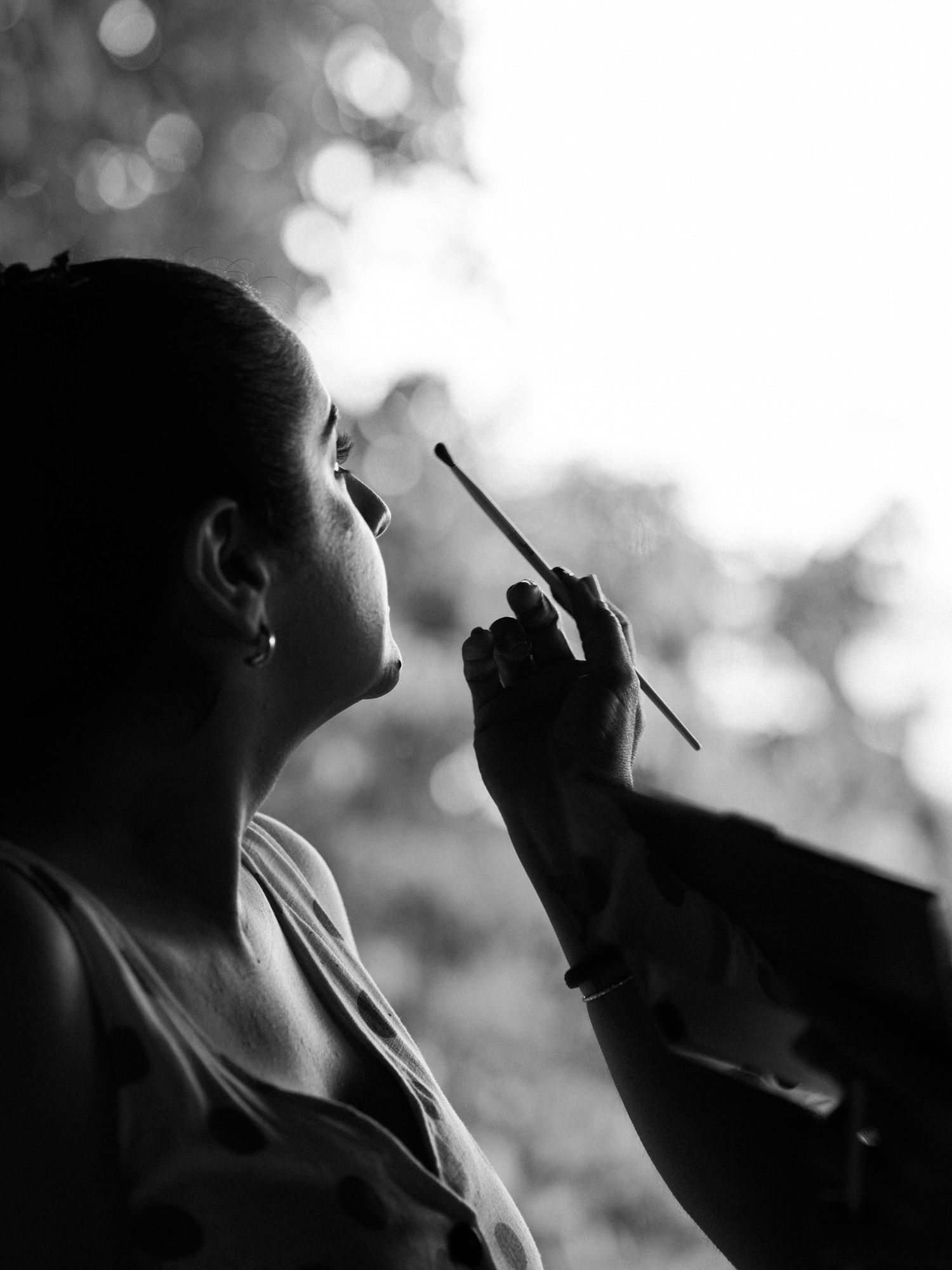 Silhouetted figures in black and white applying makeup in dramatic lighting.