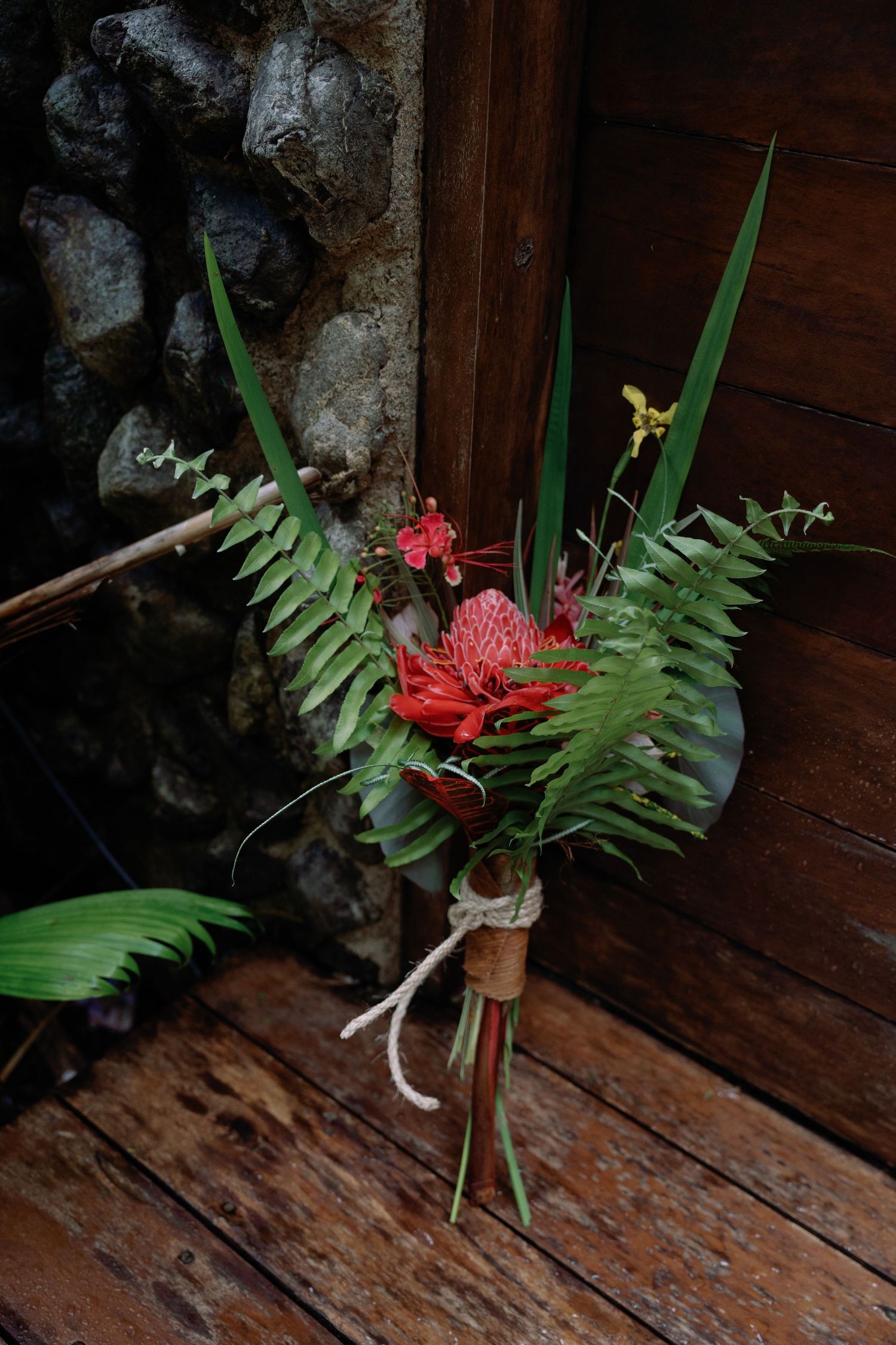 Tropical floral arrangement with red flowers and ferns on rustic wooden surface.