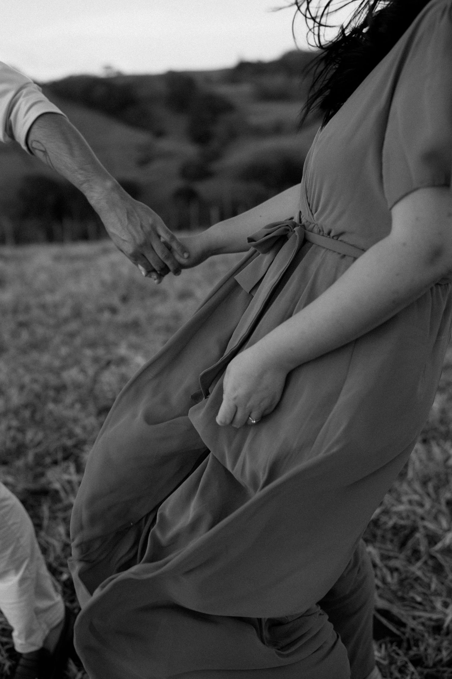Close-up details of a flowing coral dress against natural grass backdrop.