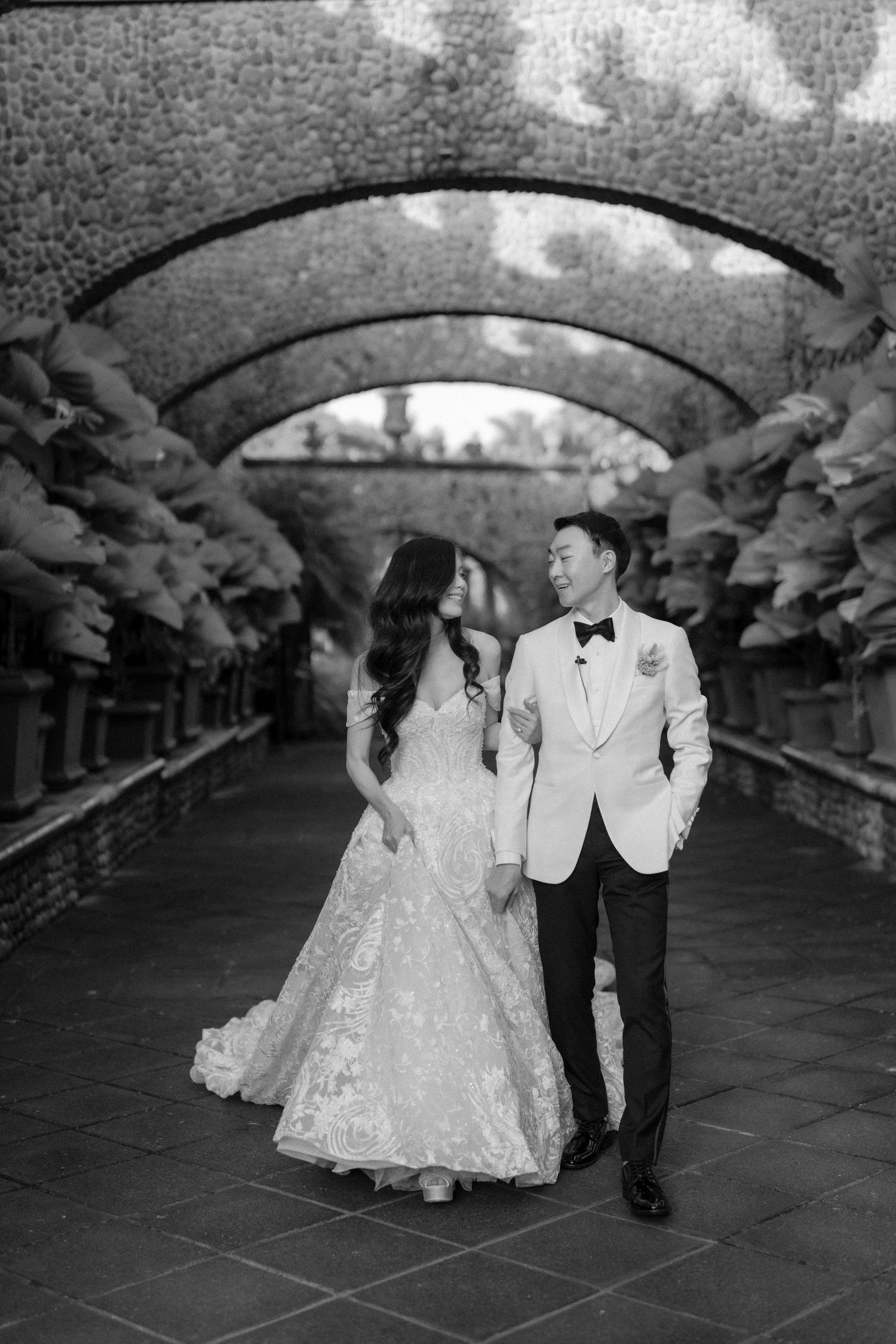 A black and white wedding photoshoot sequence showing a couple dancing under an arched bridge walkway.