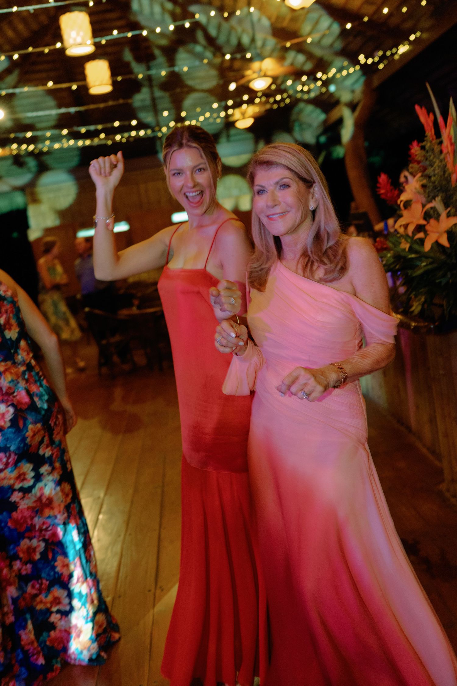 Wedding reception dance floor with guests in pink and red dresses celebrating under string lights.