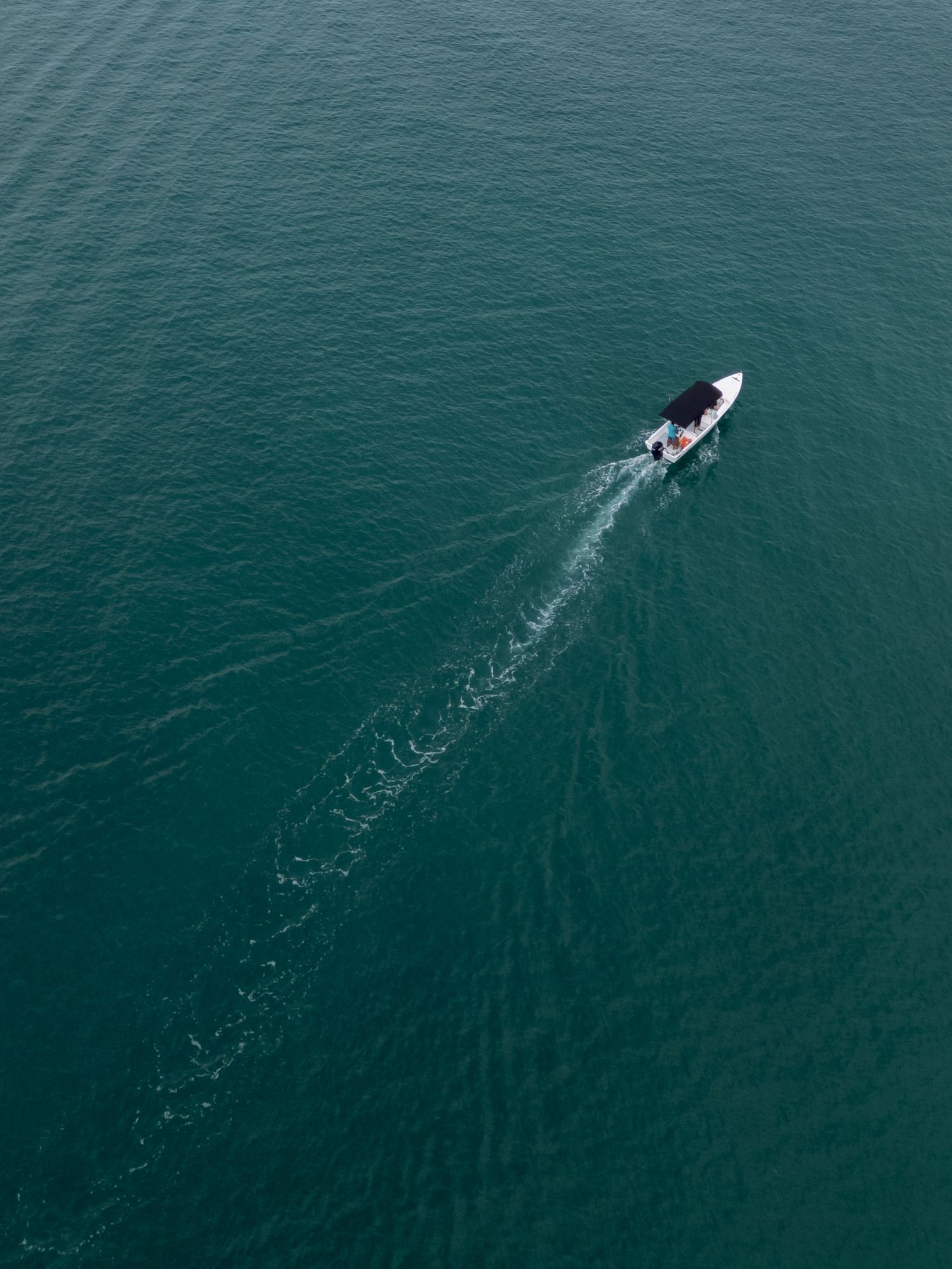 Aerial view of a small boat creating a wake in turquoise ocean waters.