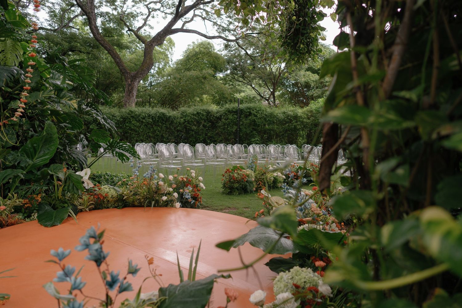 Outdoor wedding venue with chairs set up on terracotta tiles surrounded by lush greenery.
