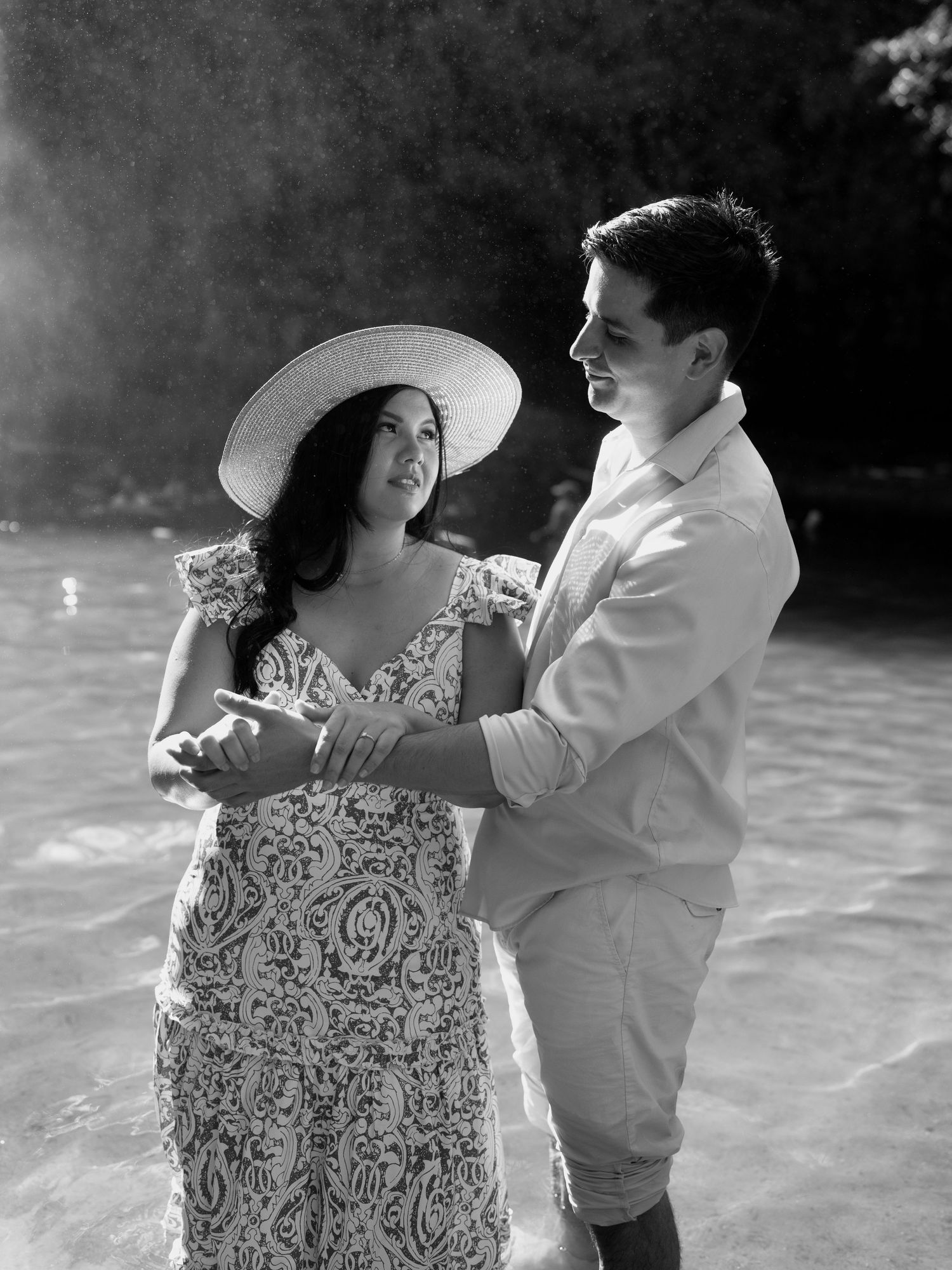 A romantic couple shares tender moments while standing in shallow water with sunlit mist in the background.