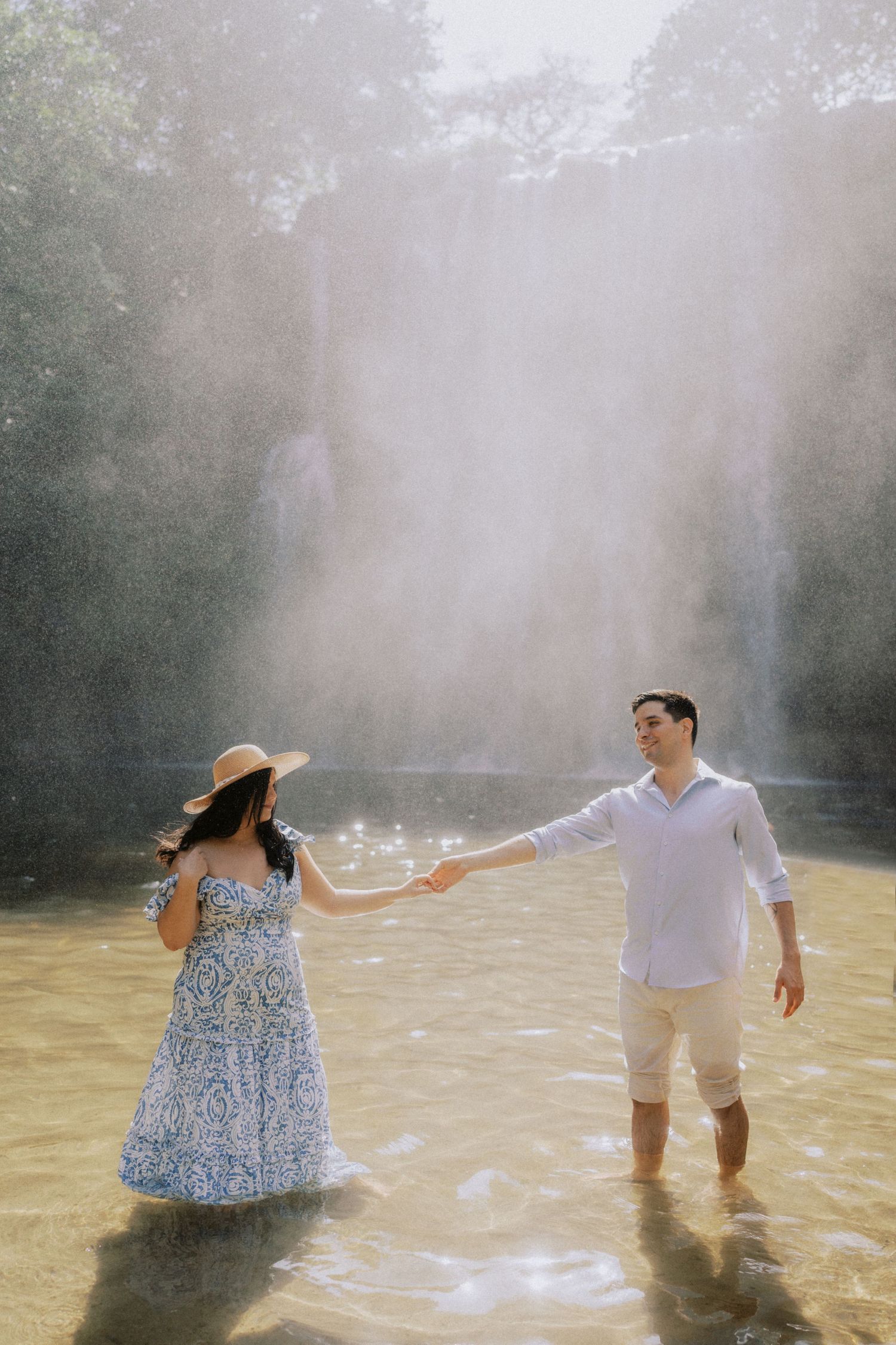 A couple plays in shallow water during a misty photoshoot, creating splashes and joyful moments.
