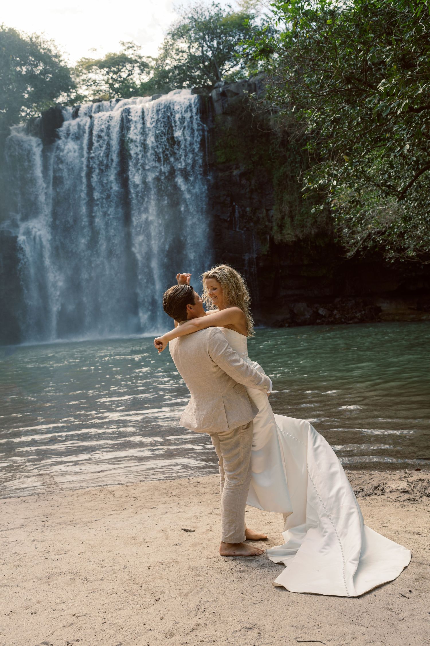 A romantic dance sequence unfolds on a beach with a dramatic waterfall backdrop.
