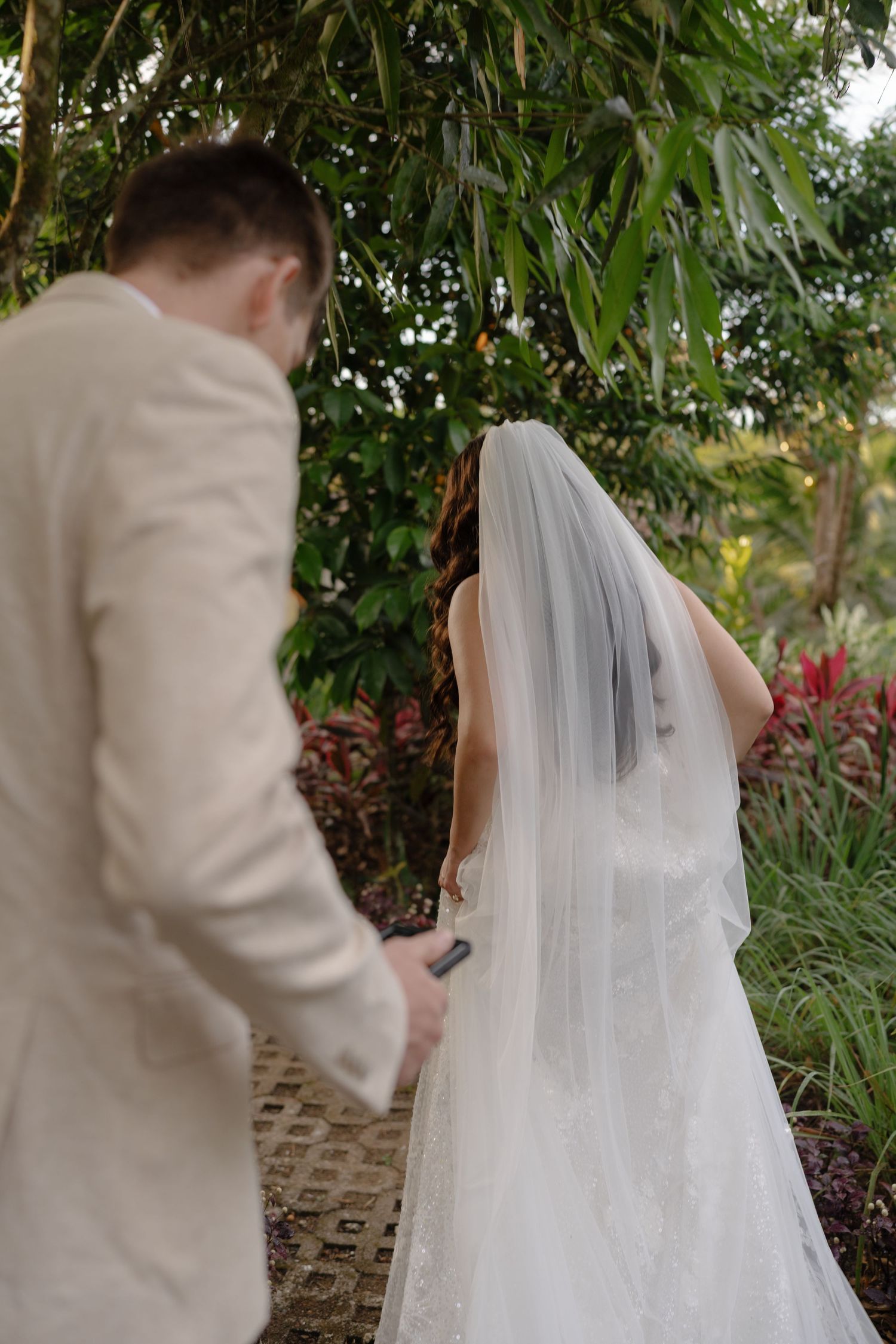 Wedding couple walking through a lush tropical garden path.