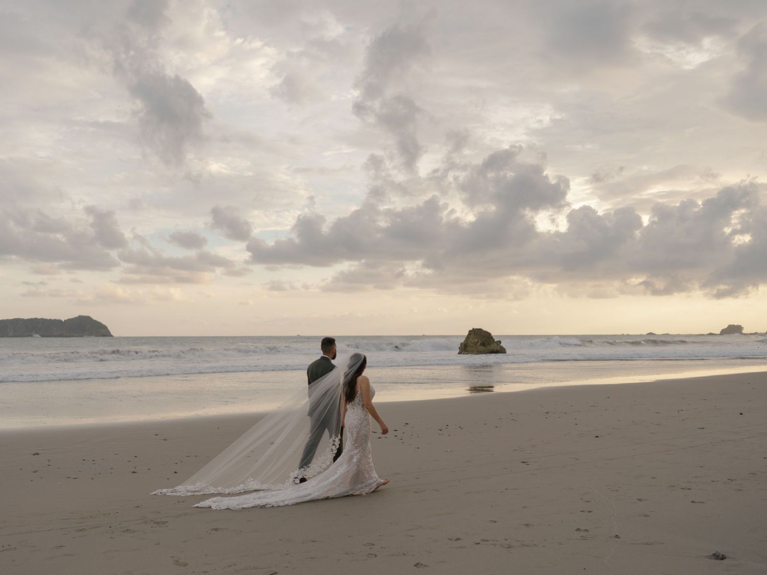 A romantic beach photoshoot with dramatic cloudy skies and ocean waves.