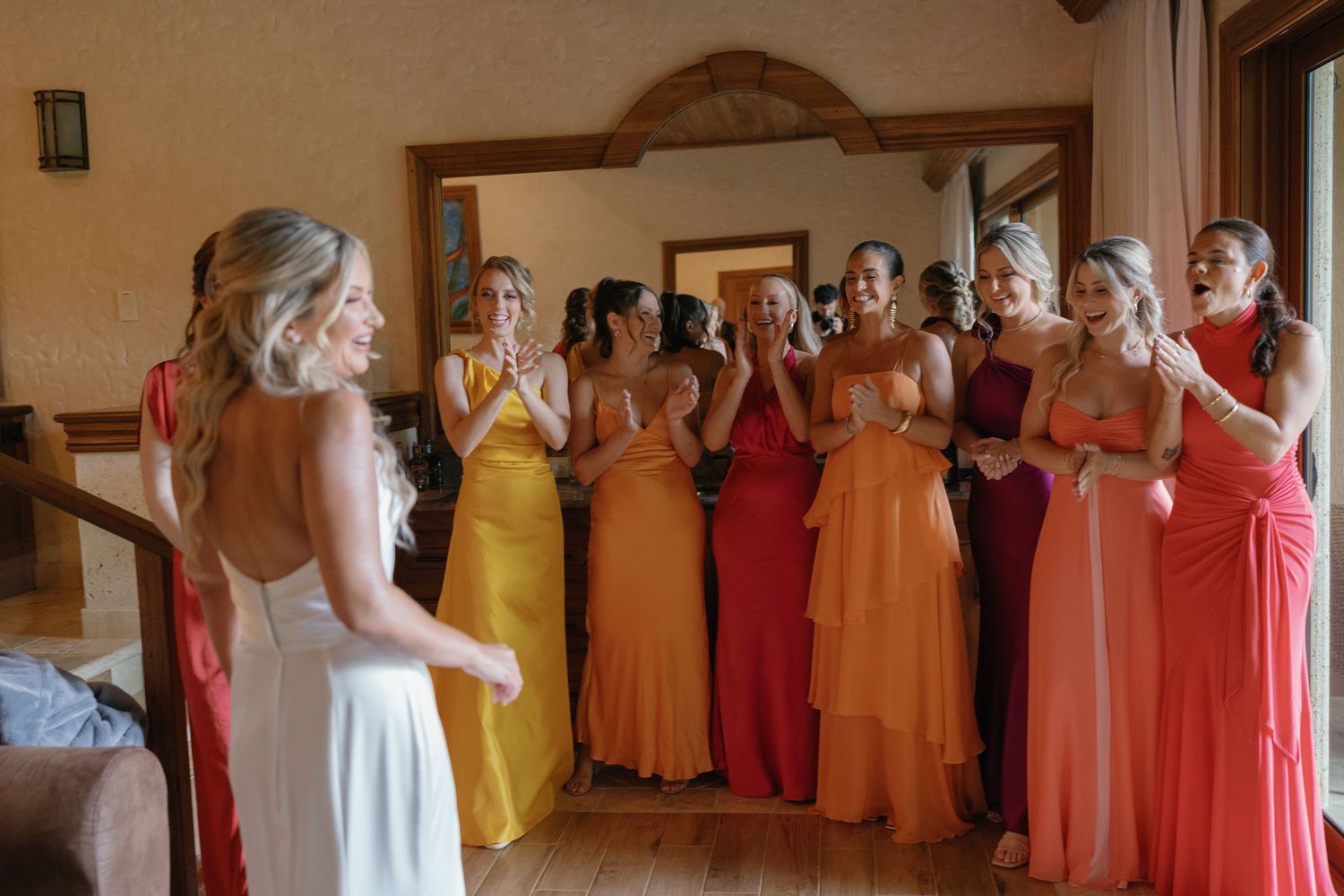 Wedding party members in colorful orange and coral dresses lined up indoors.