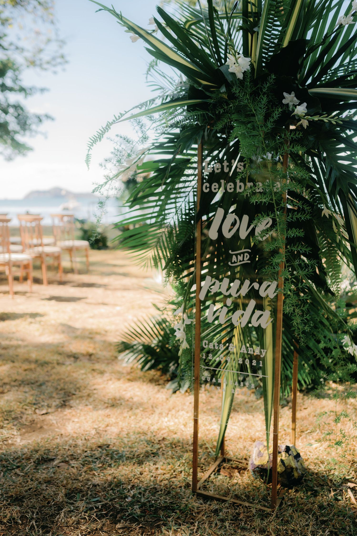 Tropical palm leaves frame wooden wedding signs in an outdoor setting.