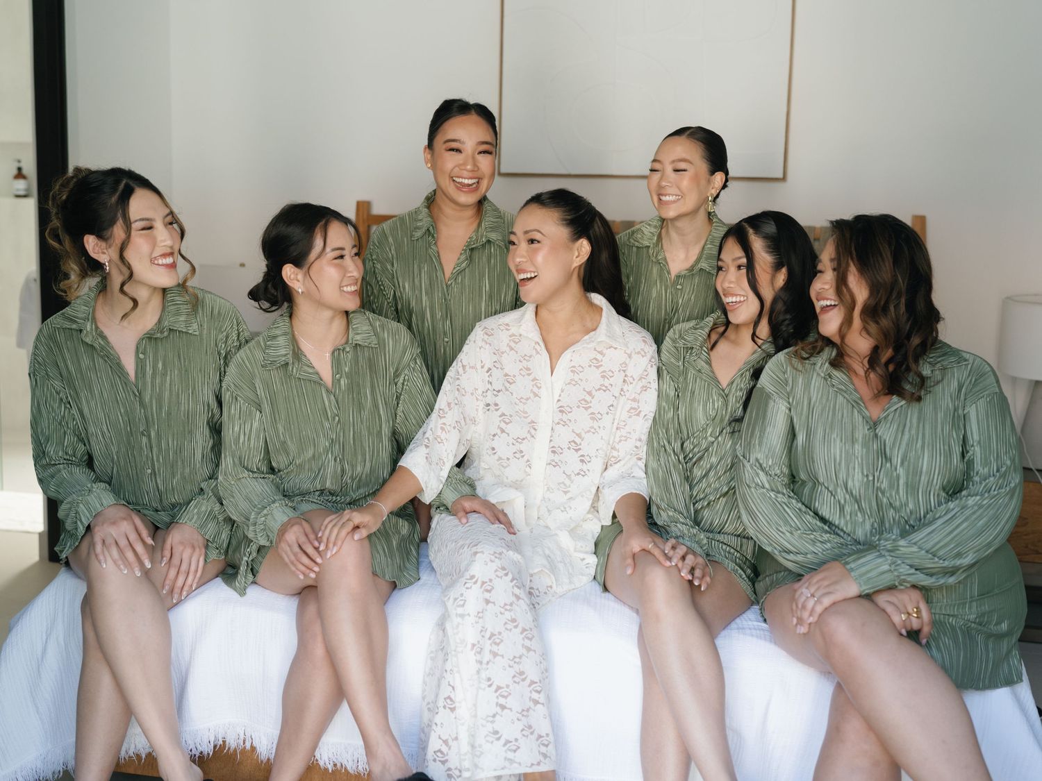 Wedding party in matching sage green robes sharing laughter during pre-ceremony preparations.