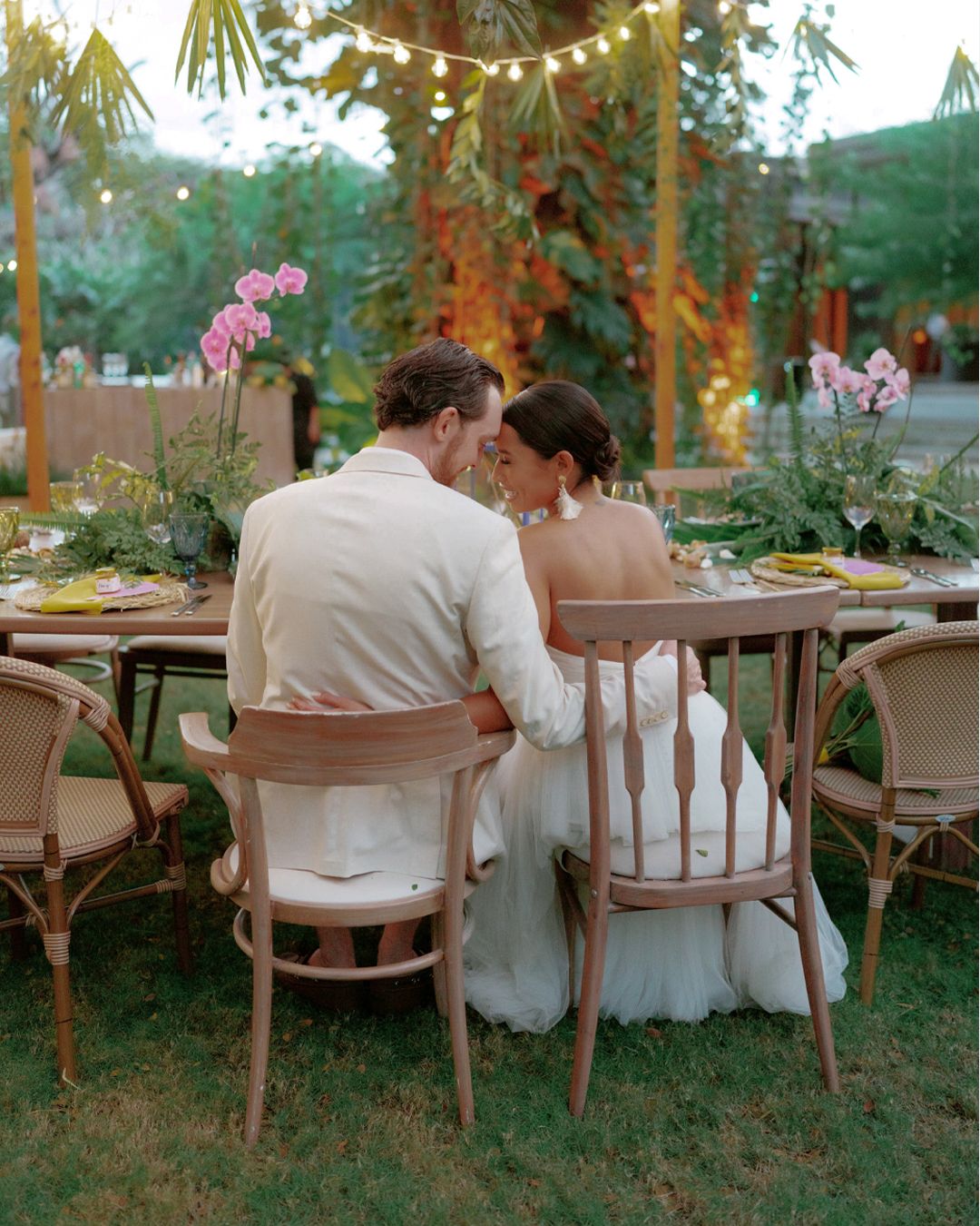 An elegant outdoor wedding reception setup with string lights and floral arrangements at dusk.