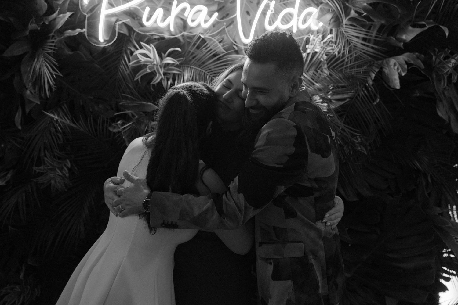 Neon 'Pura Vida' sign glowing against dark tropical foliage at night.