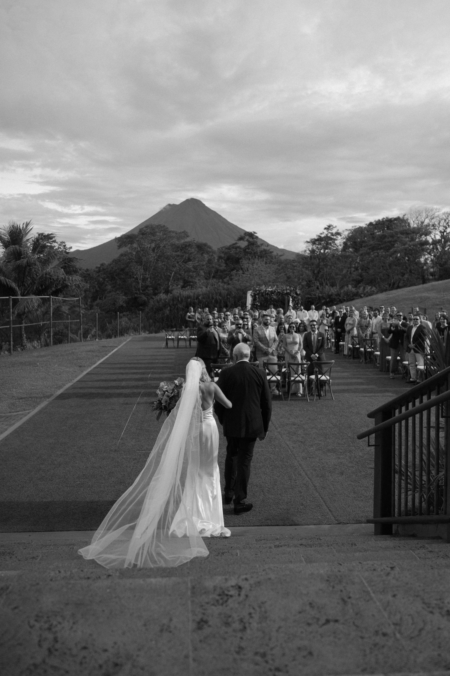 Outdoor wedding ceremony with mountain backdrop and dramatic cloudy sky.