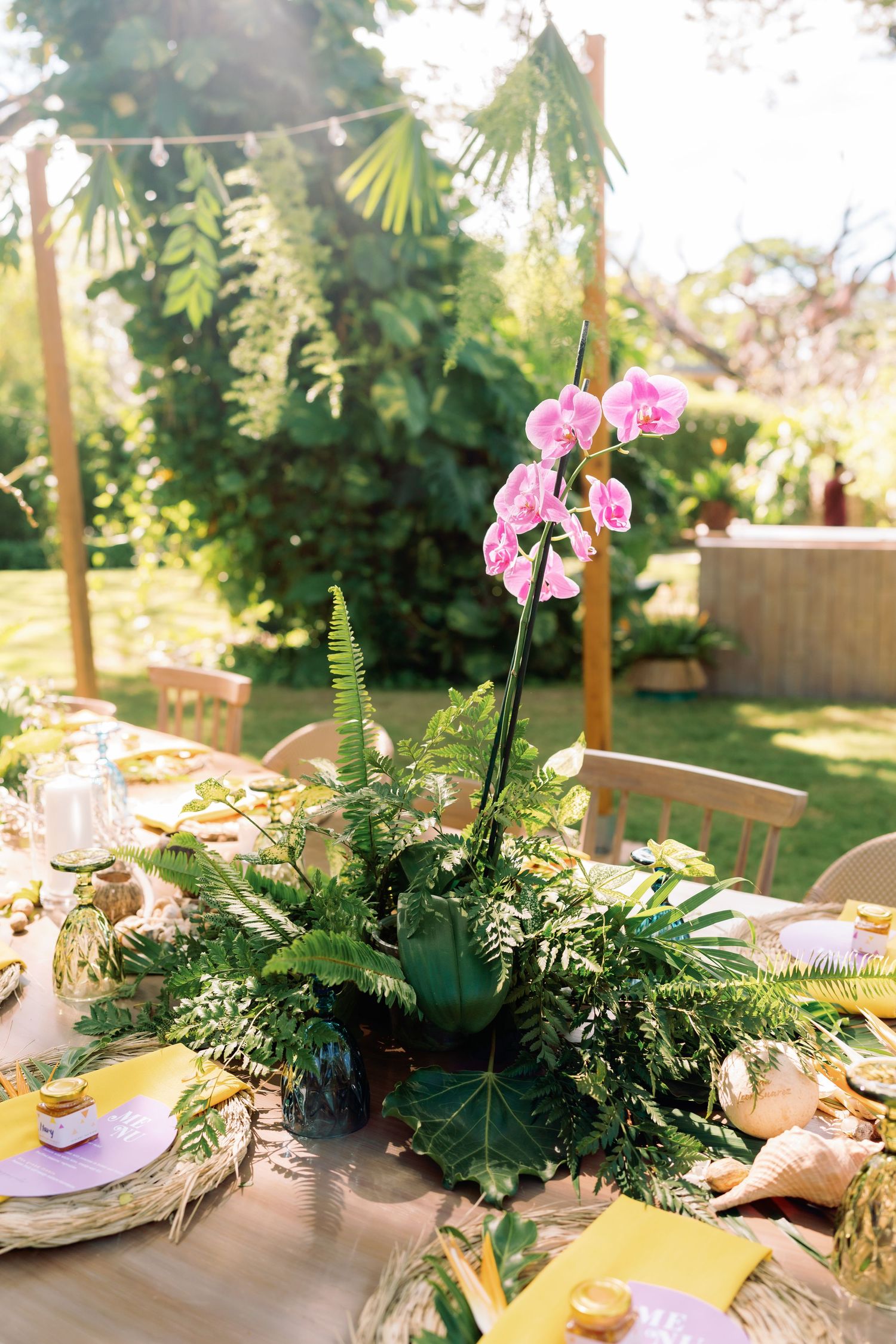 Table centerpieces featuring pink orchids and ferns at a tropical-themed wedding reception.
