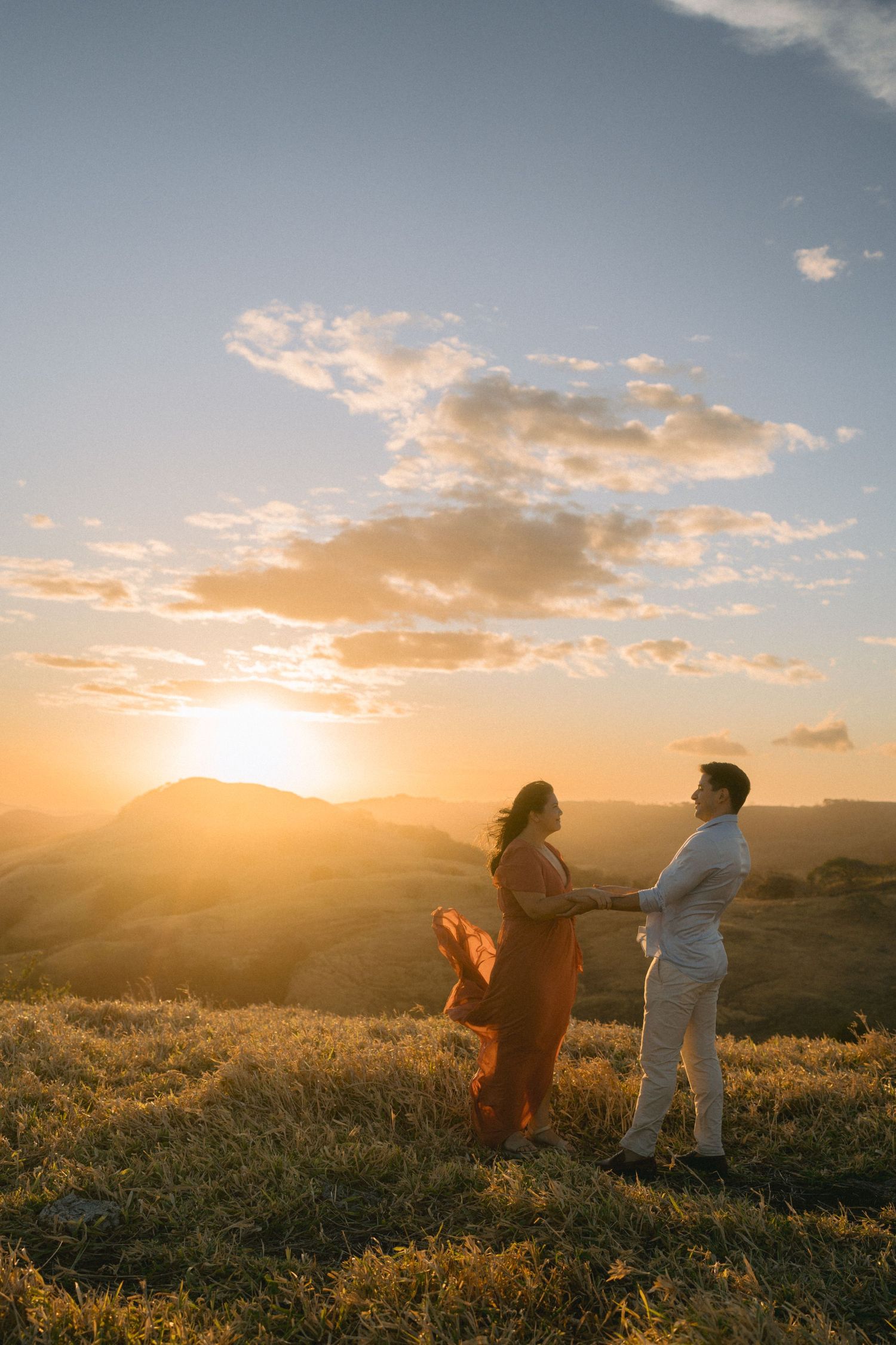 Two people in contrasting outfits dance in a field during golden sunset.