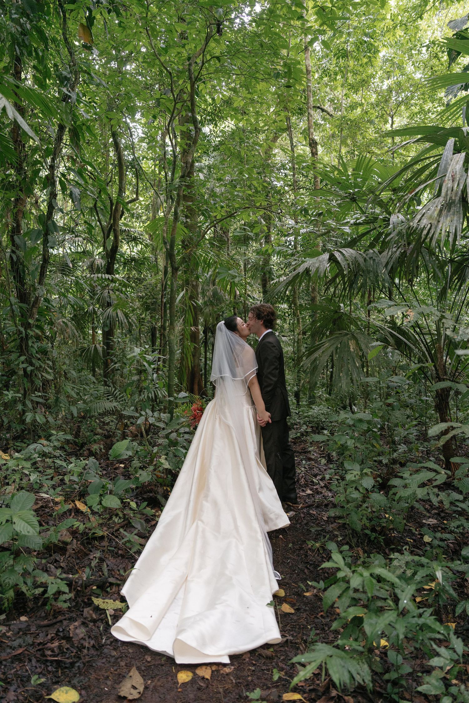 A romantic wedding photoshoot in a lush tropical forest setting with towering trees.