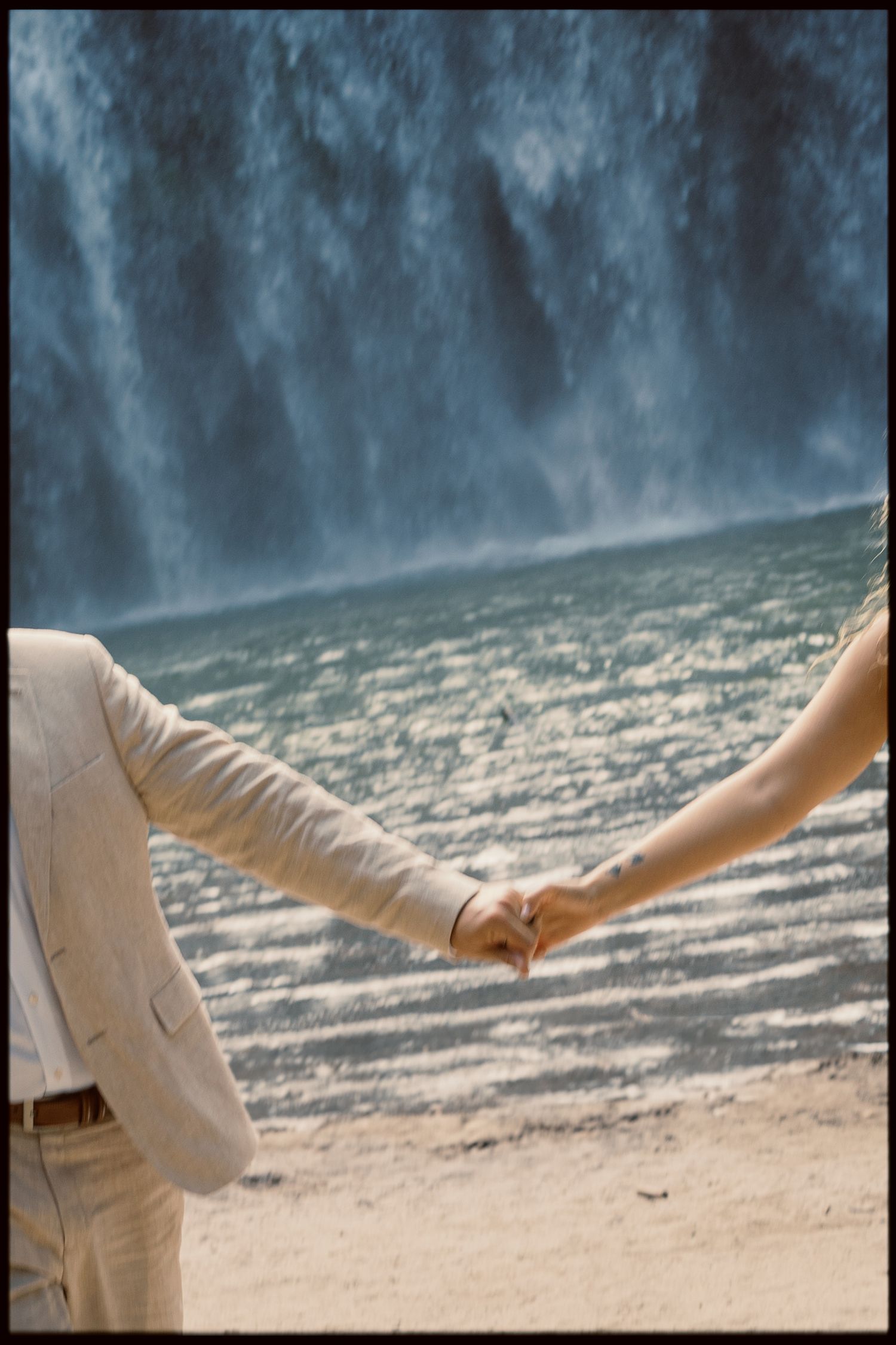 Hands reach out in an artistic pose against the misty backdrop of a cascading waterfall.