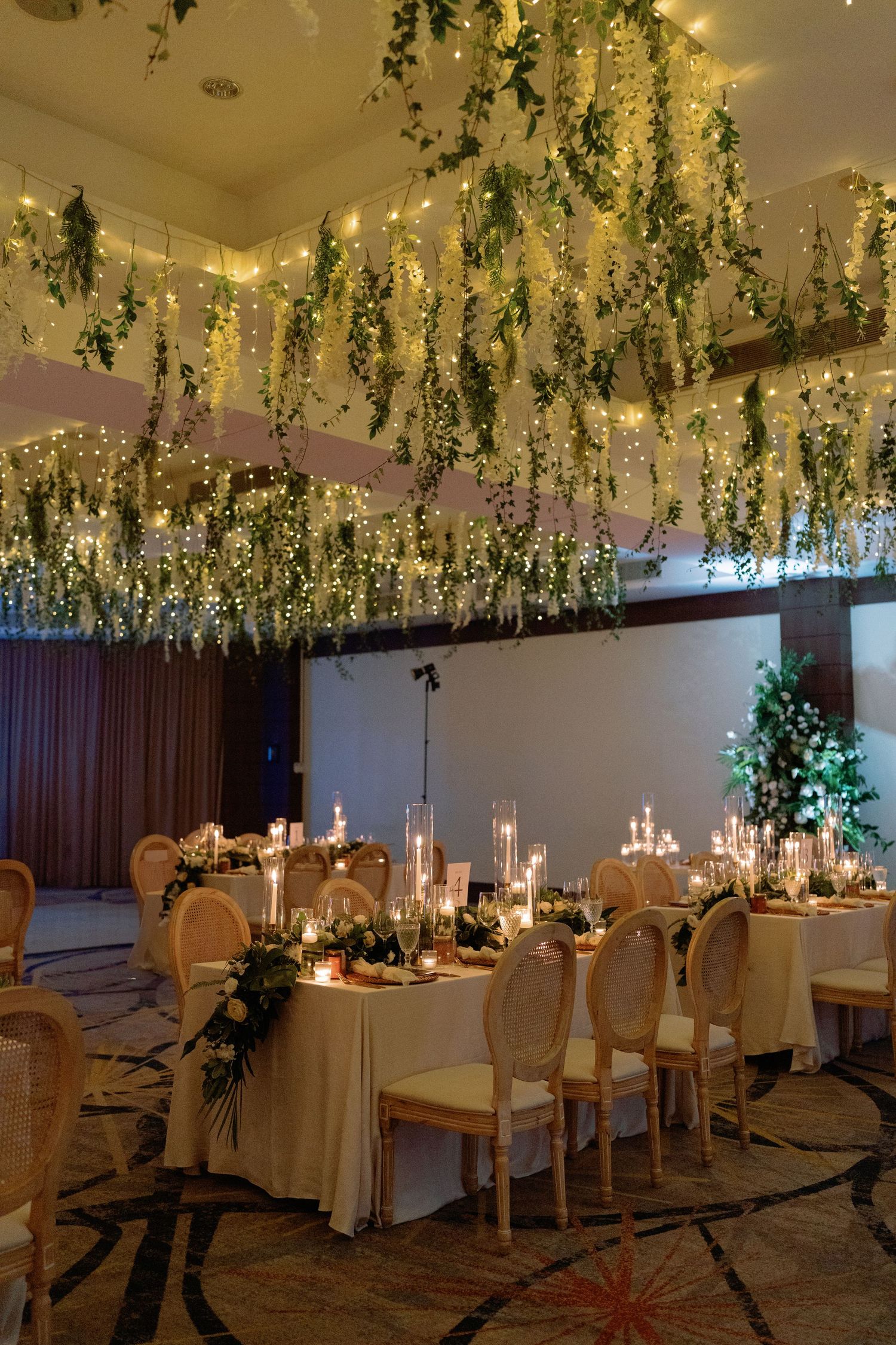 Elegant indoor wedding reception venue with hanging floral decor and candlelit tables creating a romantic atmosphere.