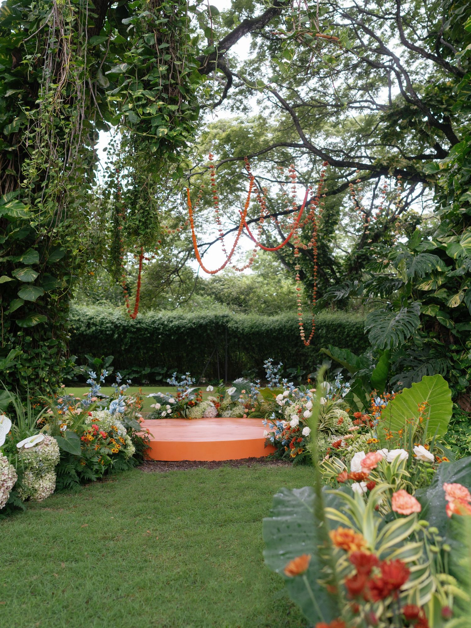 Tropical garden setting with orange flowers and lush greenery for outdoor wedding ceremony.