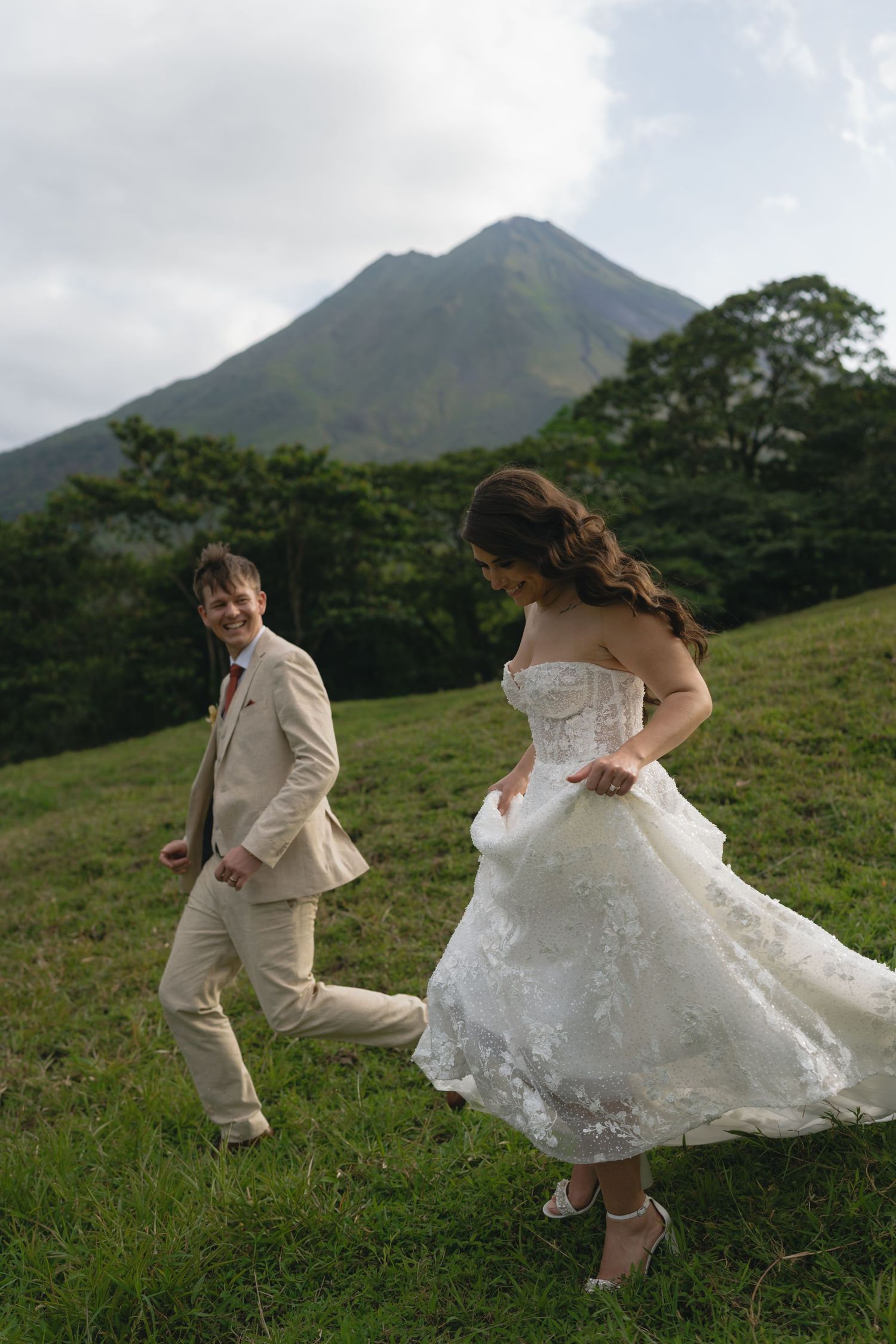 Playful newlyweds dancing and twirling in a grassy field with mountains in the background.