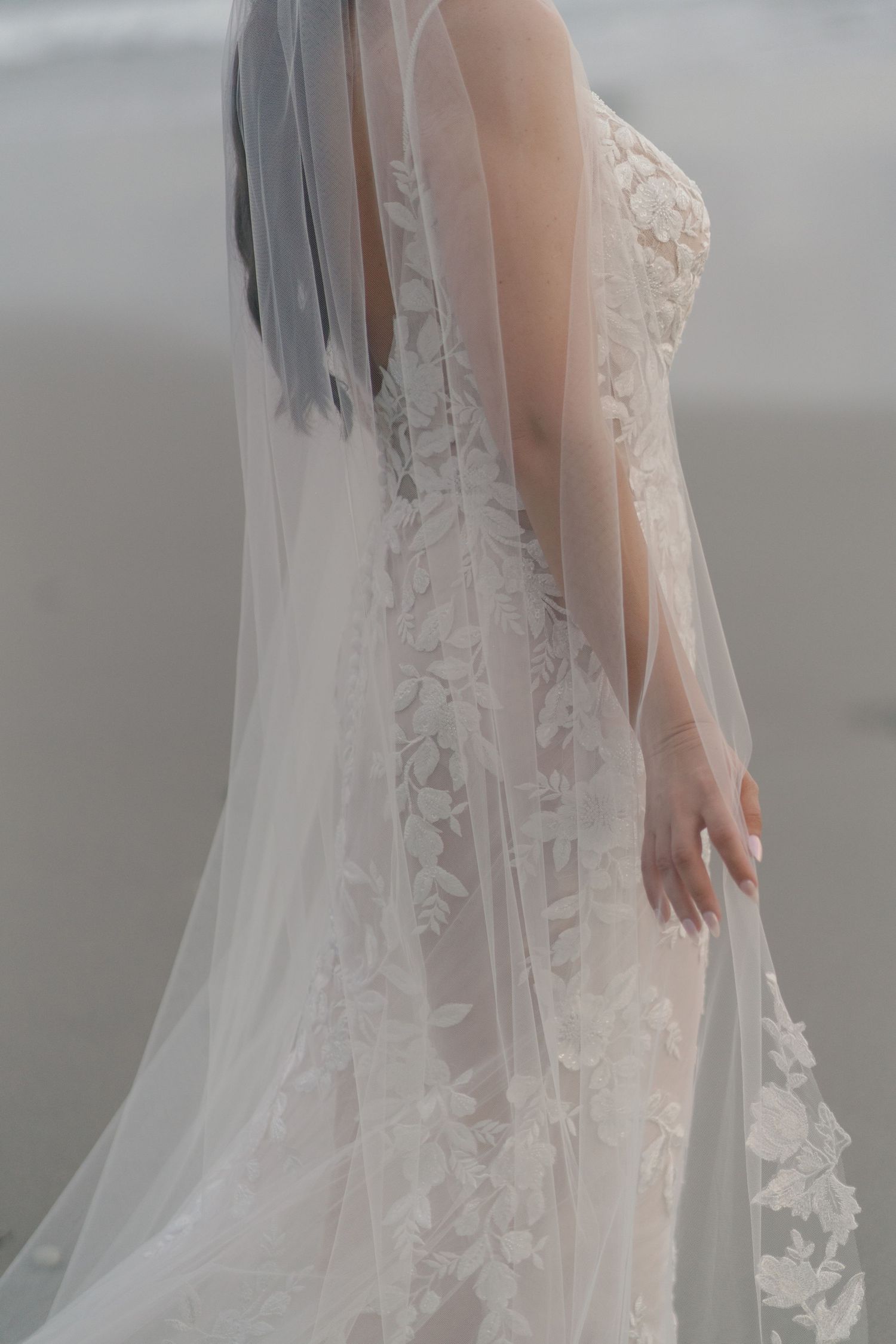 Close-up detail of delicate lace wedding dress with flowing veil.