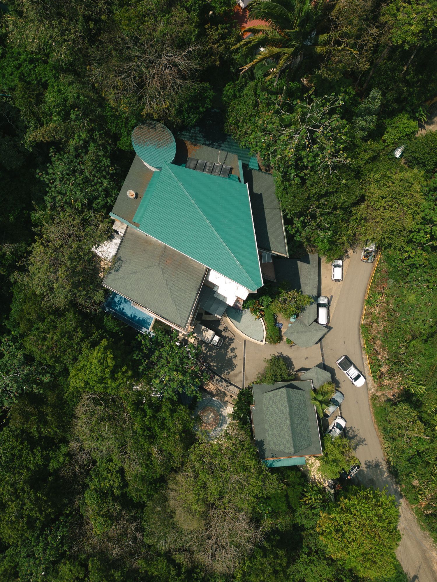 Aerial view of tropical buildings with teal roofs surrounded by lush vegetation.