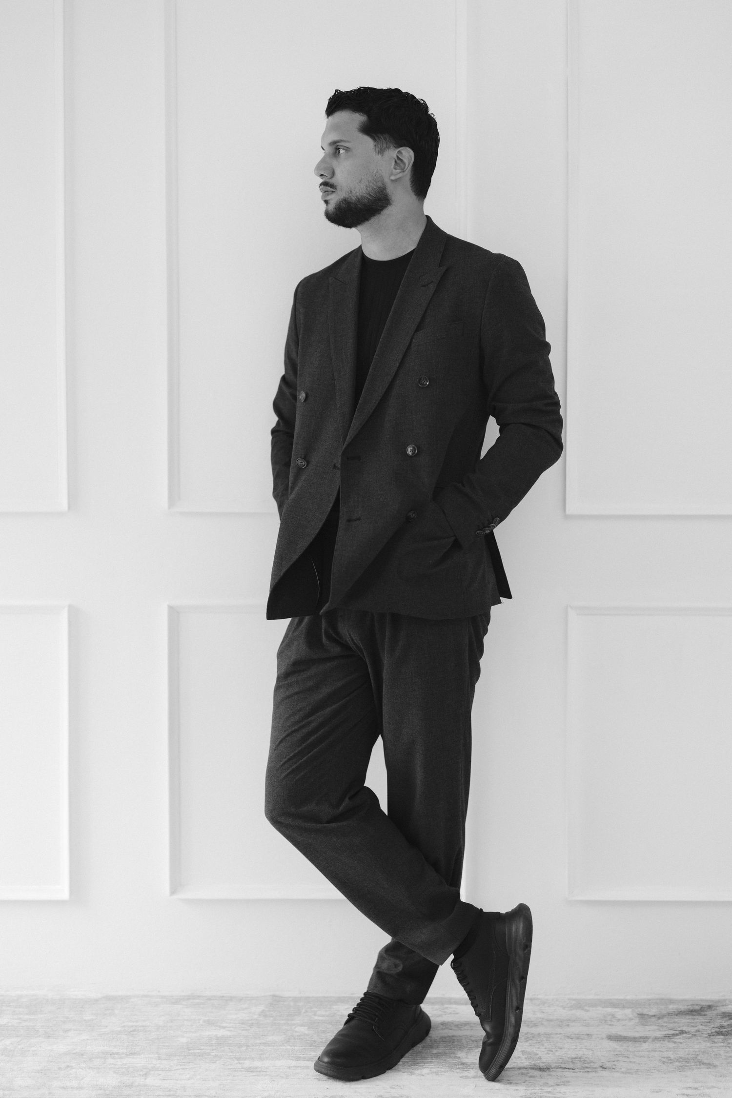 A black and white photo series showing a person in a dark suit striking different poses against a white wall.