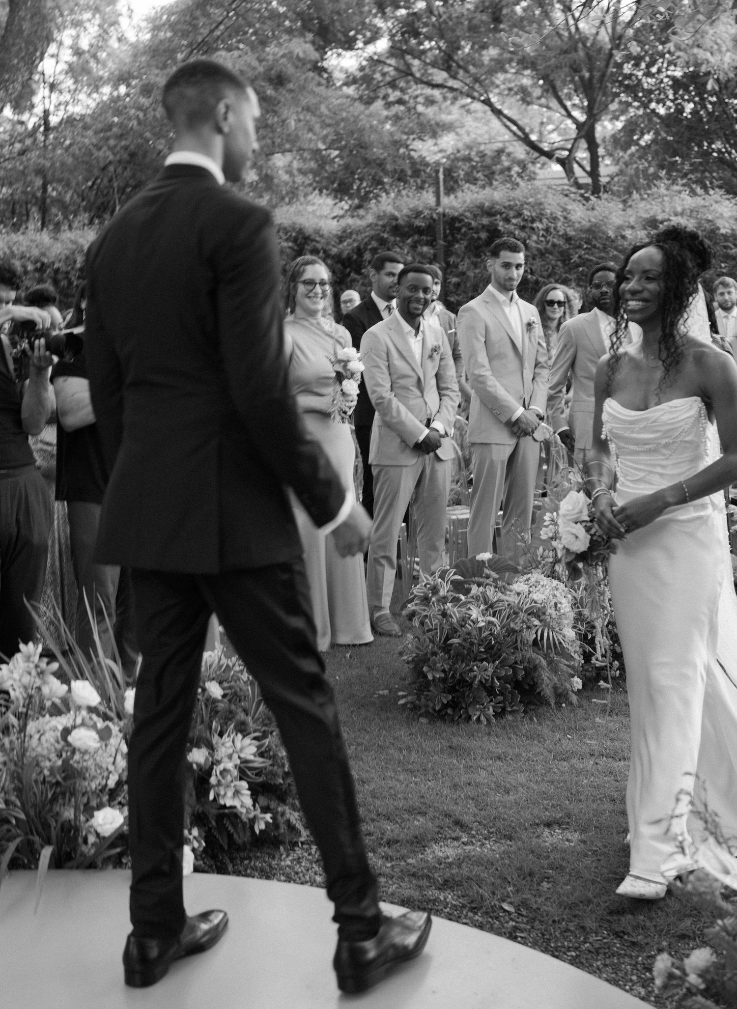 Wedding ceremony guests gathered outdoors in a garden setting.