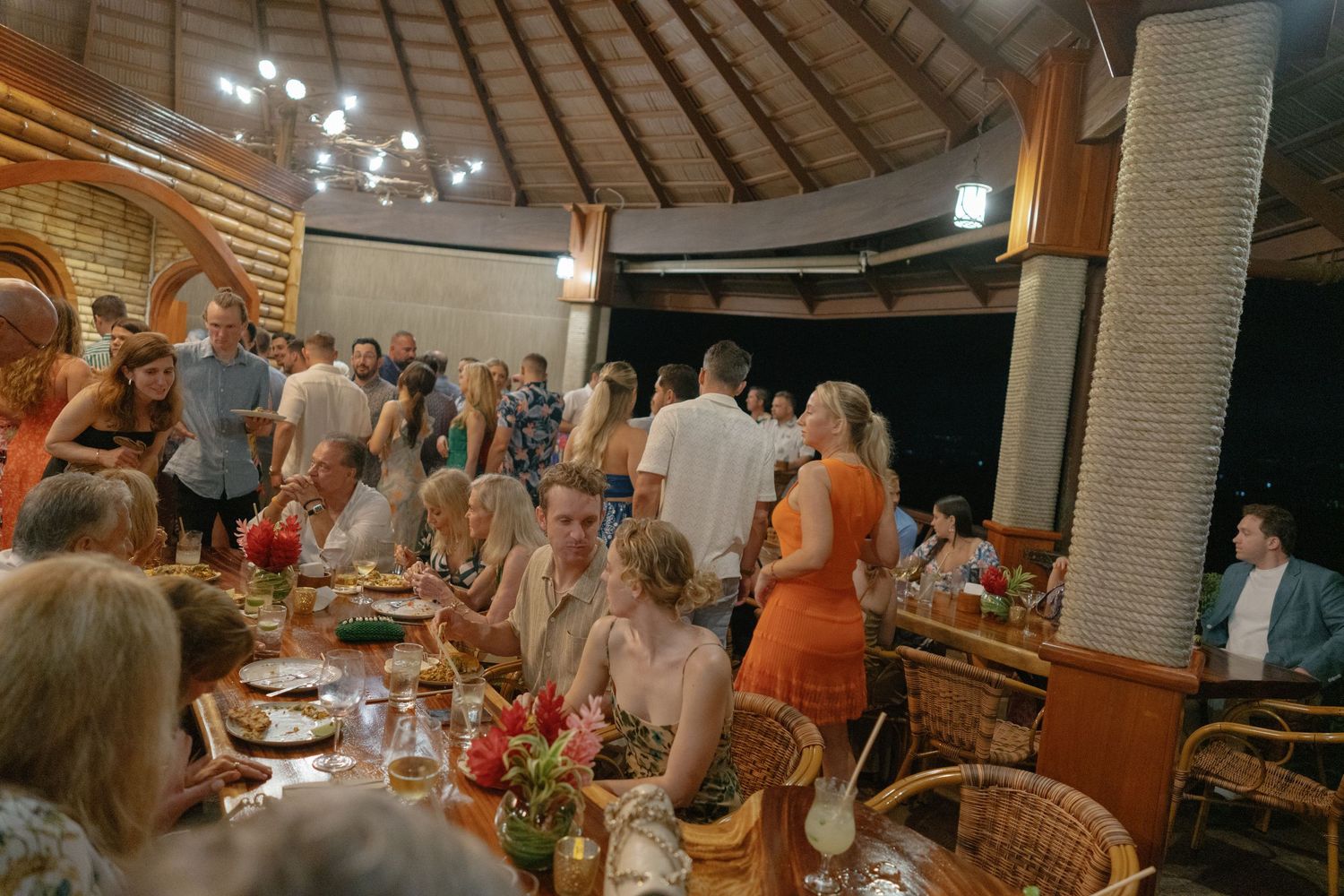 Guests gather for a celebration dinner under a vaulted ceiling with warm lighting and elegant table settings.